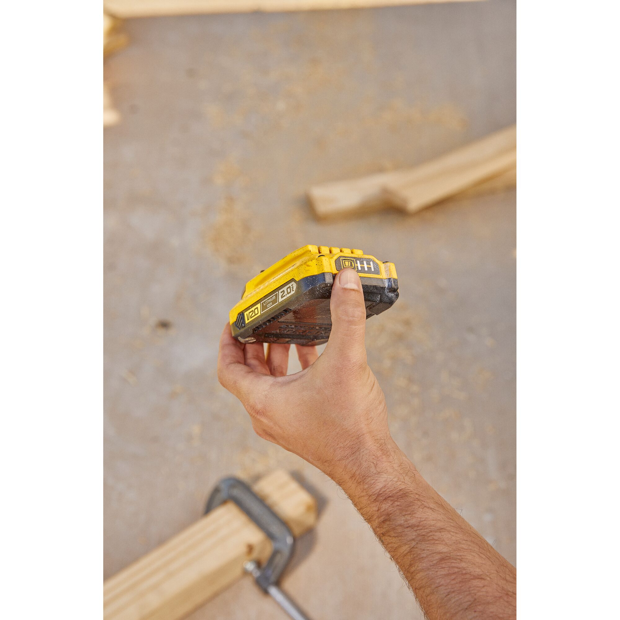 Photography of STANLEY SB202 V20 2.0Ah battery held in hand at a woodworking workspace.