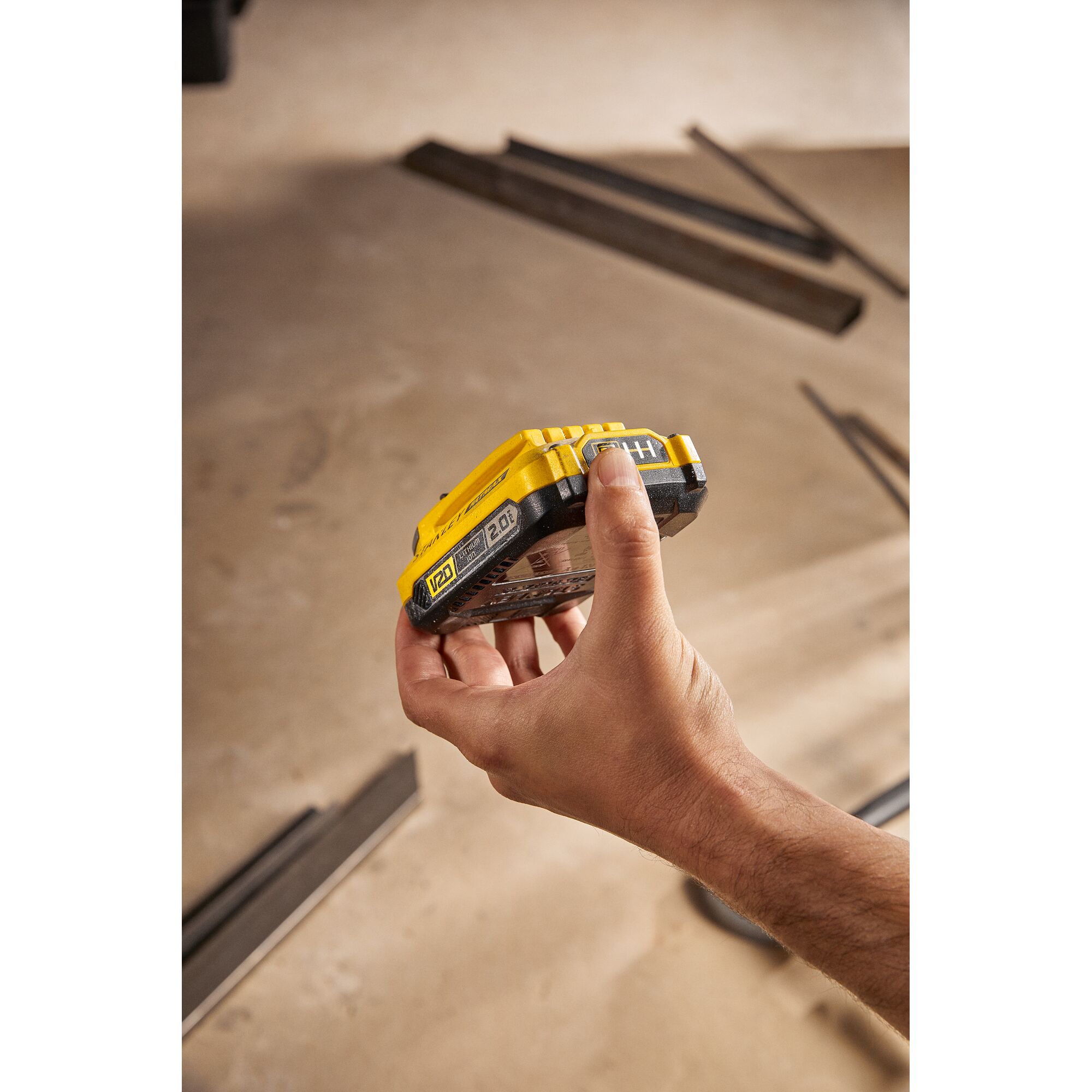 STANLEY SB202 battery held in hand, yellow and black, V20 series, shown in workshop setting.
