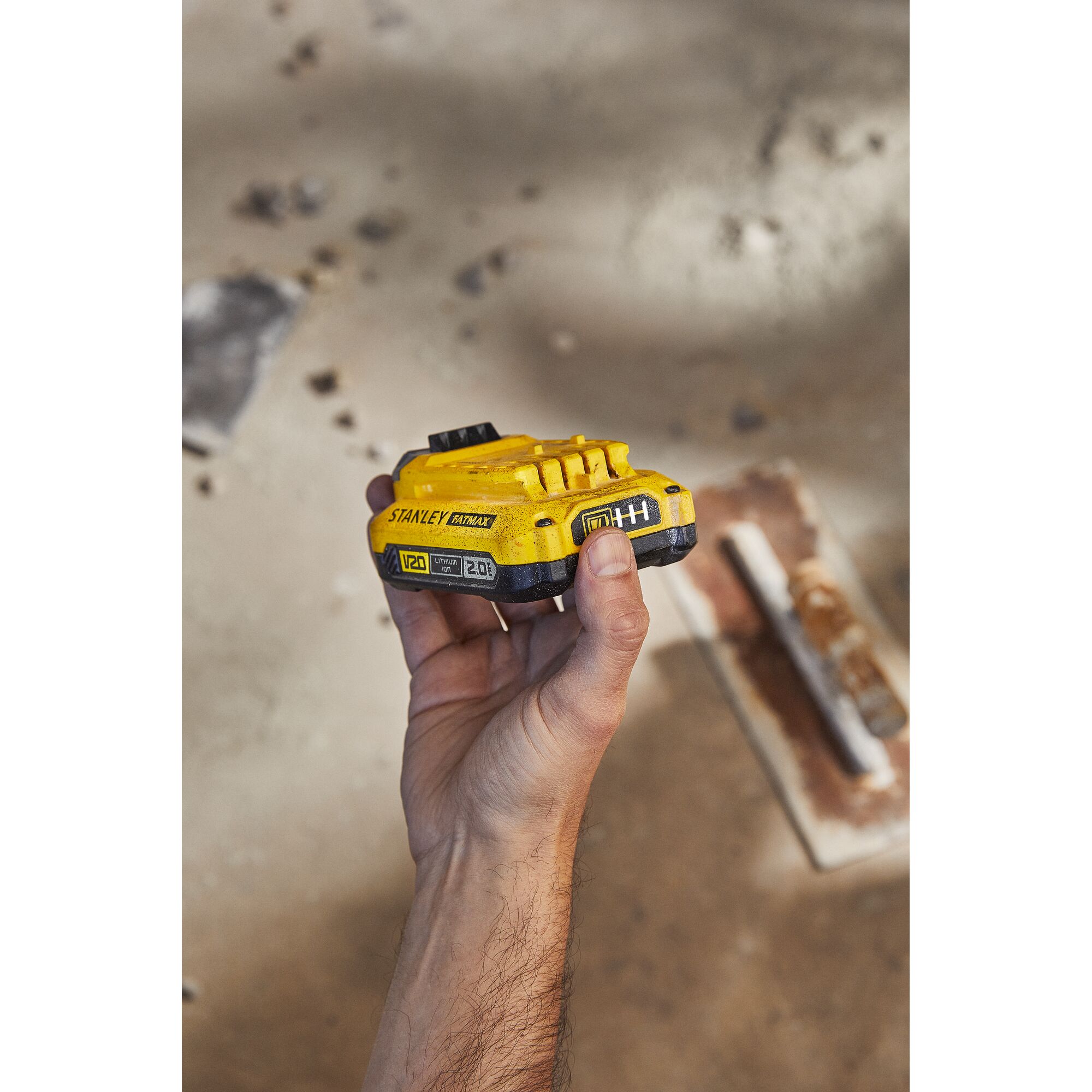 Stanley SB202 battery held in hand, yellow V20 lithium-ion, photography on construction site.