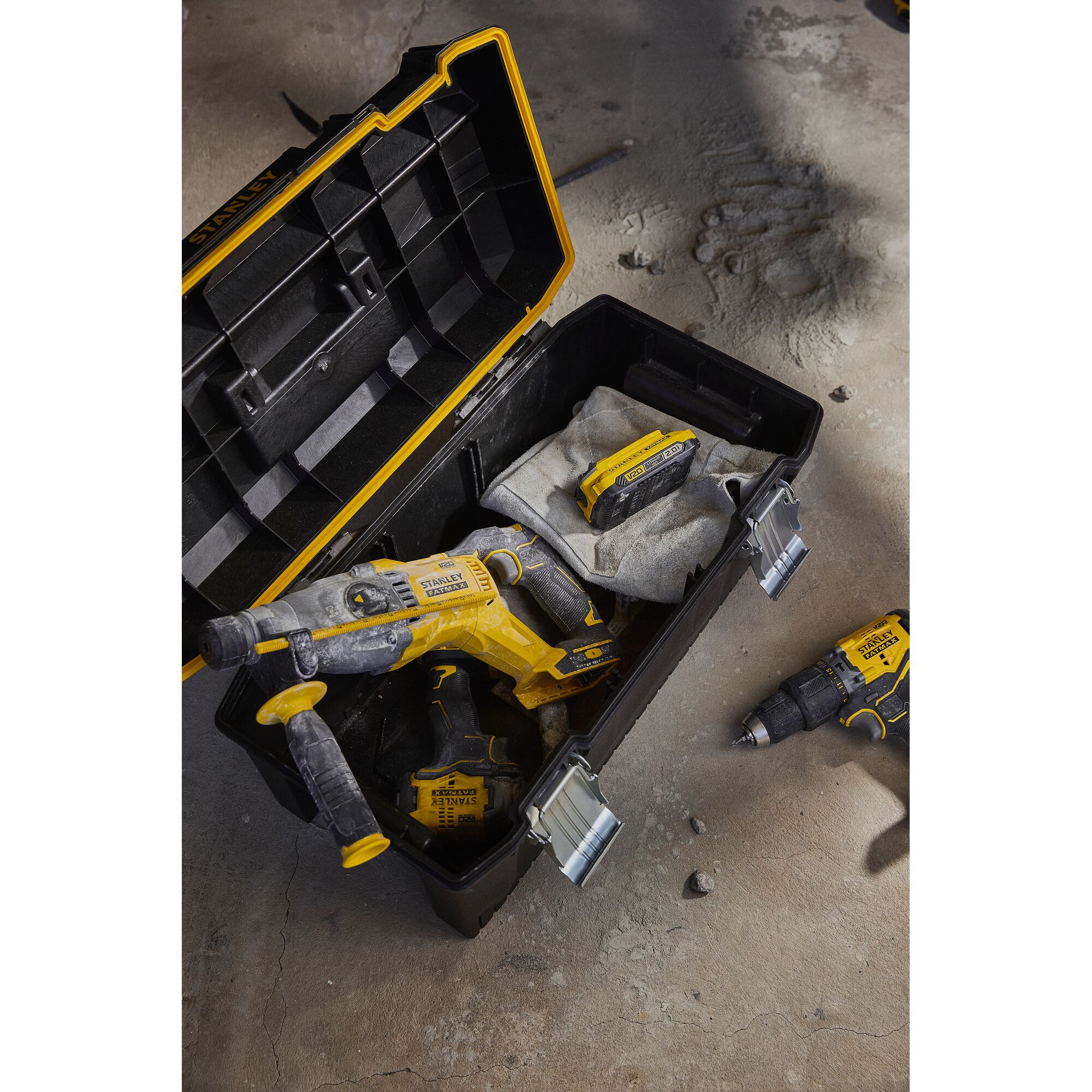 STANLEY SB202 photography of a yellow tool box with power tools and batteries on a dusty concrete floor.