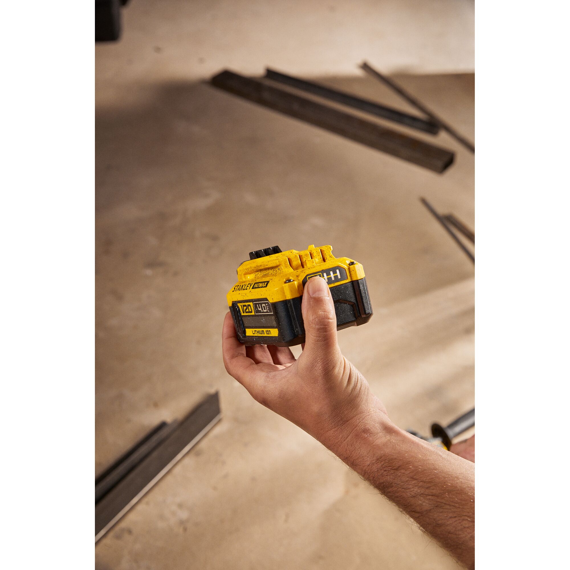 Photo of STANLEY SB204-KR 20V lithium-ion battery held in a hand, construction materials in background.