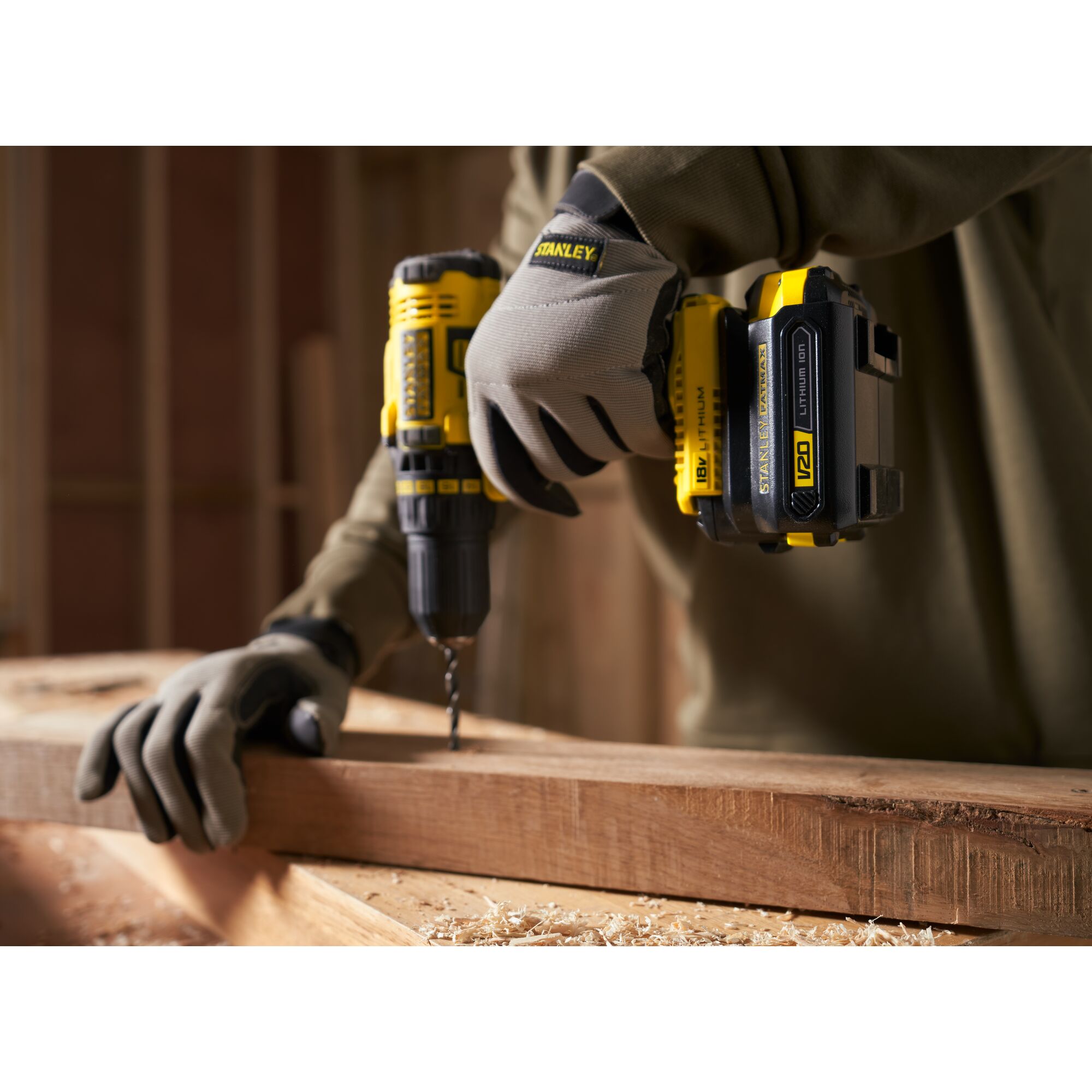 Stanley SBA100 cordless drill in use, closeup, on wood beam with user wearing Stanley gloves.