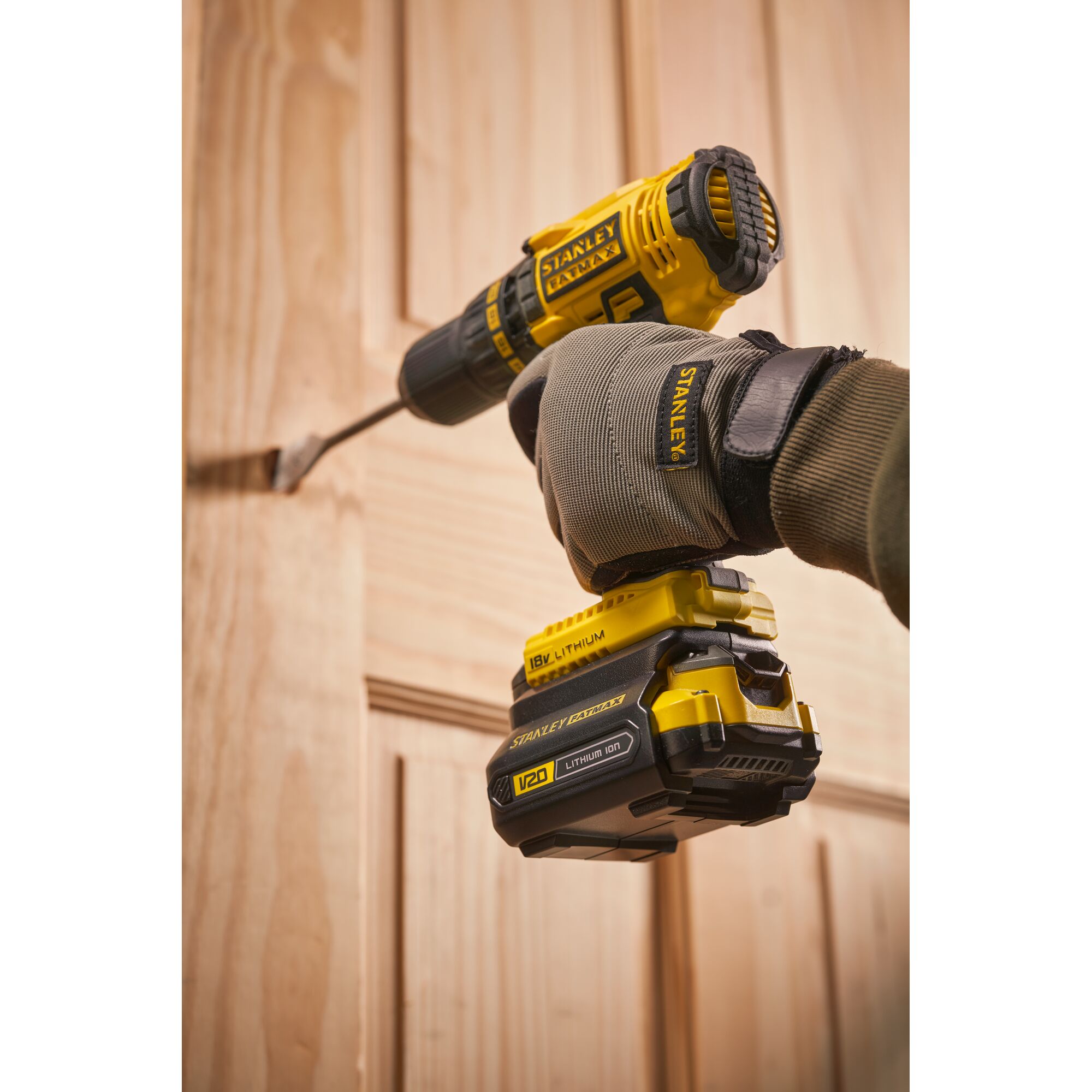 Photo of STANLEY SBA100 cordless drill in use drilling into a wooden door, close-up angle, yellow and black tool.