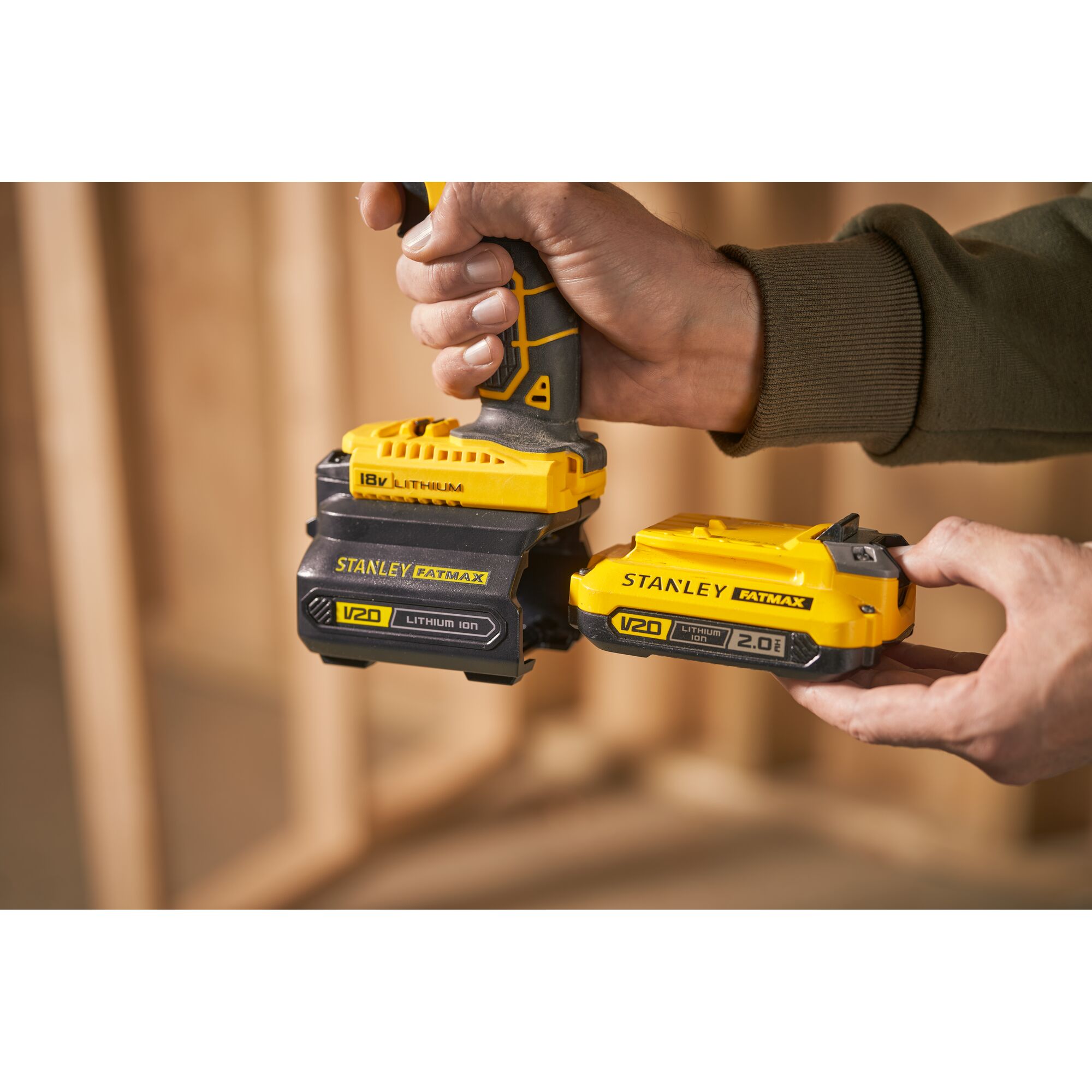 STANLEY SBA100 V20 Lithium Ion battery pack held in hand, close-up, with tool and background out of focus.