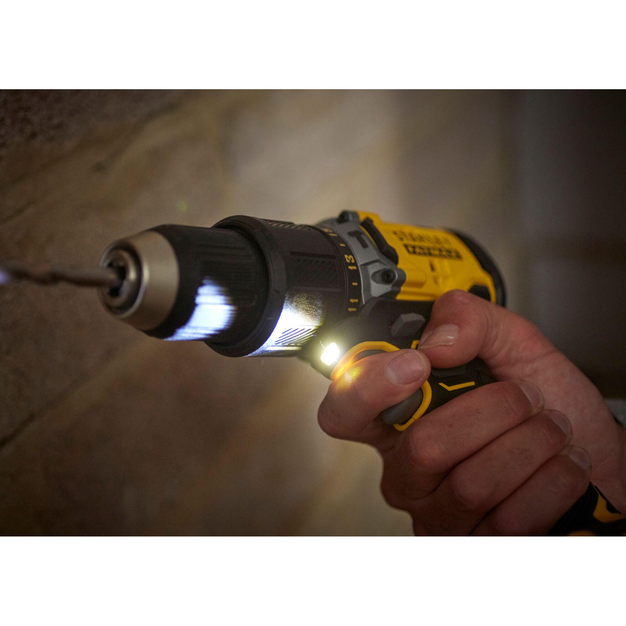 STANLEY SBD715D2K cordless drill photography, yellow and black tool with LED light drilling into wall.