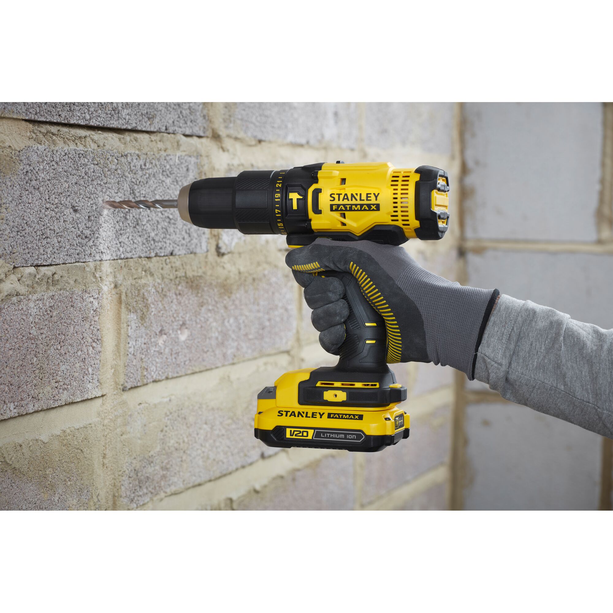 Stanley SCD711C1H-B2 cordless drill in use on masonry wall, side angle, yellow and black design.