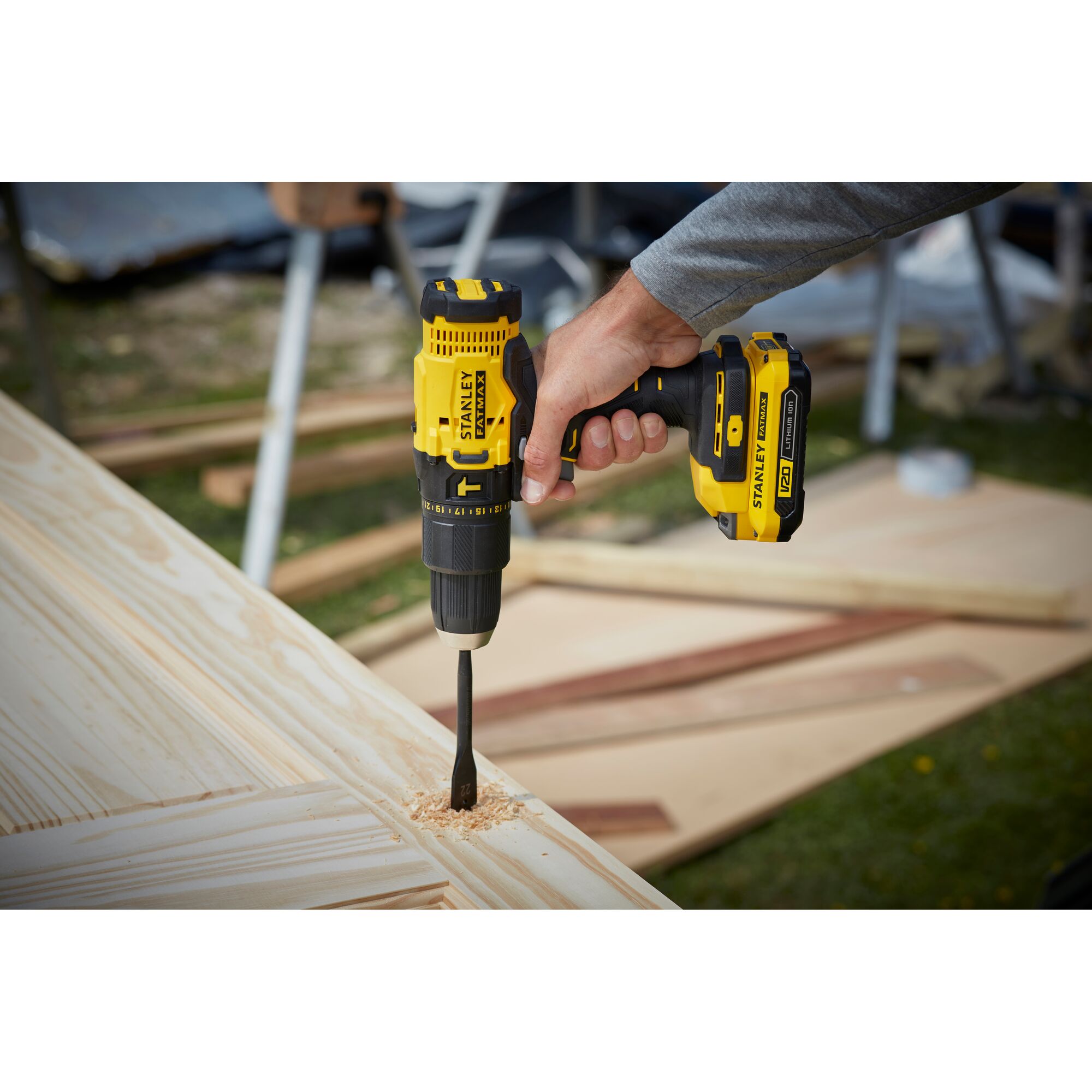 Stanley SCD711C1H-B2 cordless drill in use, drilling a hole in a wooden board outdoors.
