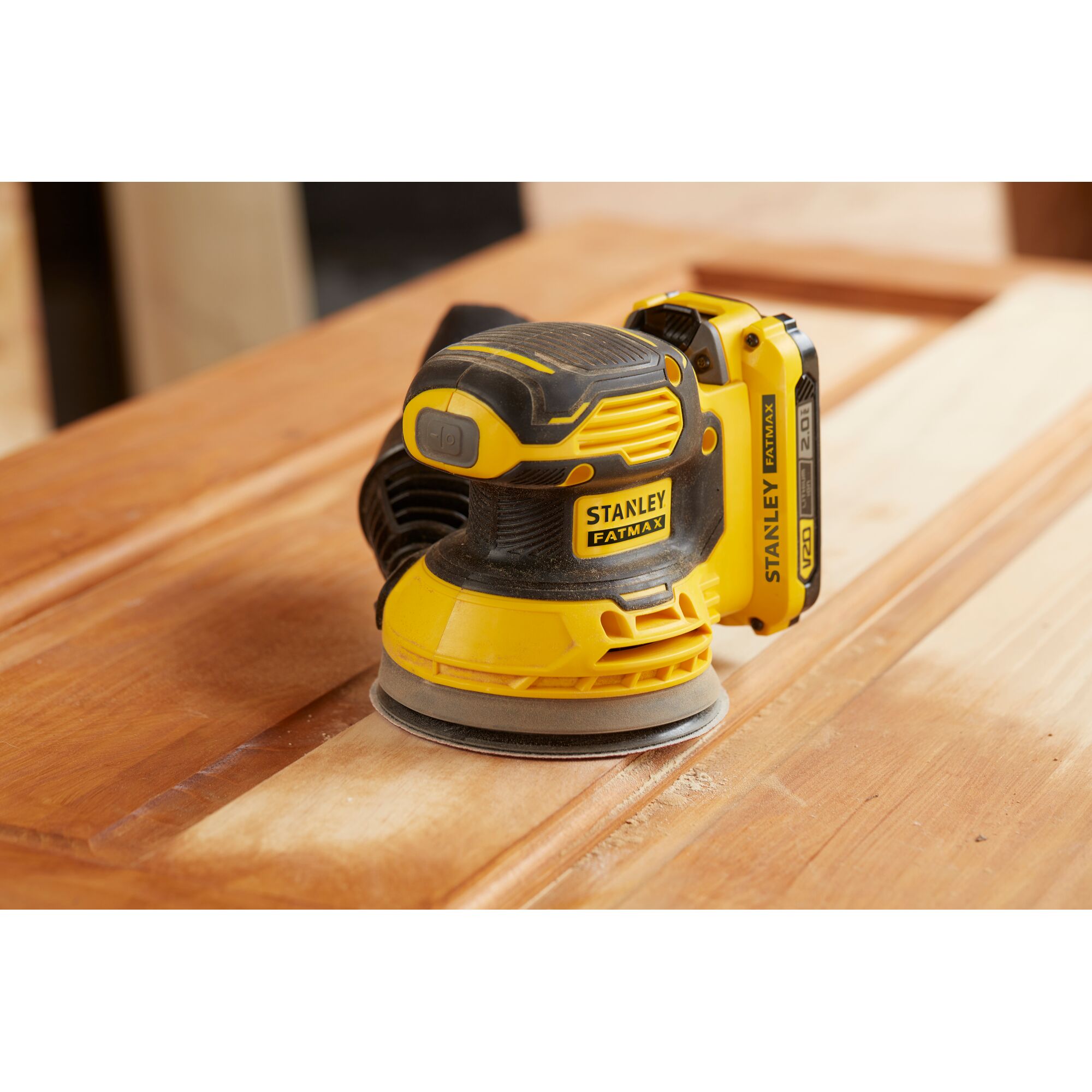 Stanley SCS220B cordless random orbital sander in use on wood surface, side angle.