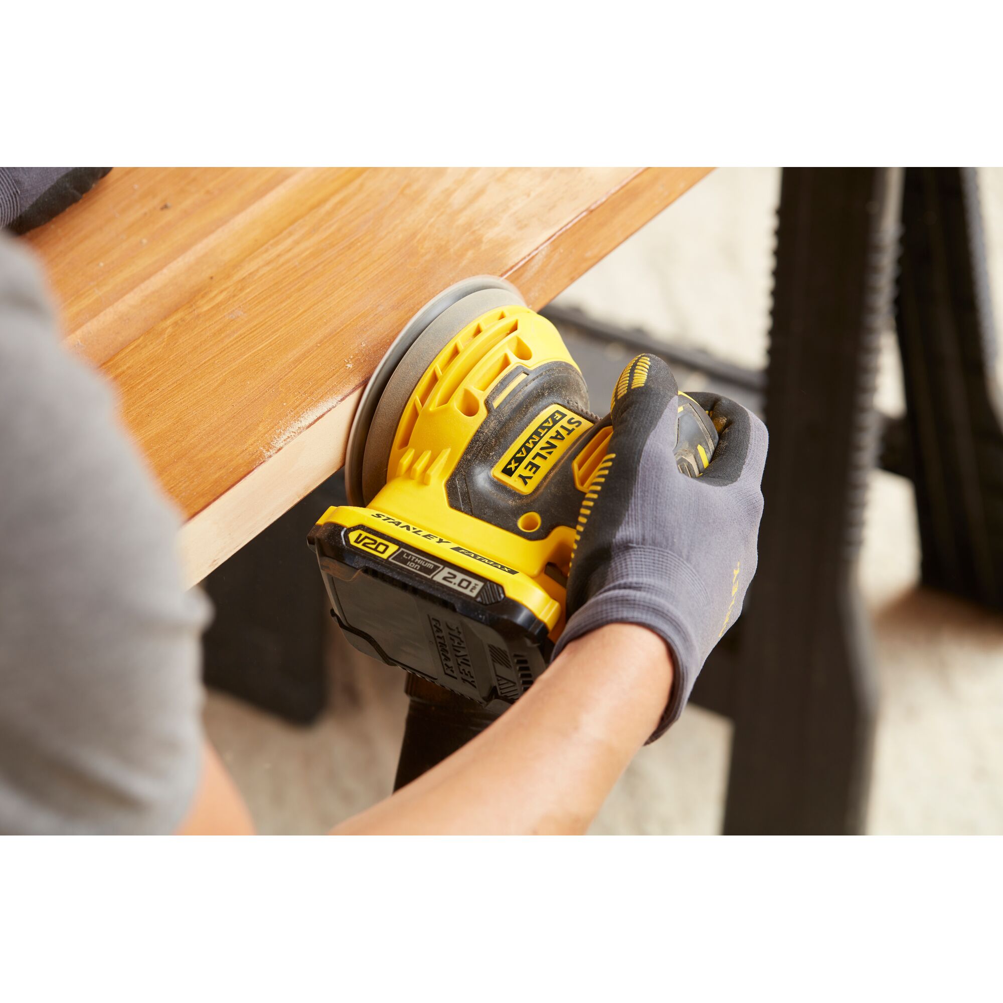 Stanley SCS220B cordless sander used on wood surface, close-up angle.