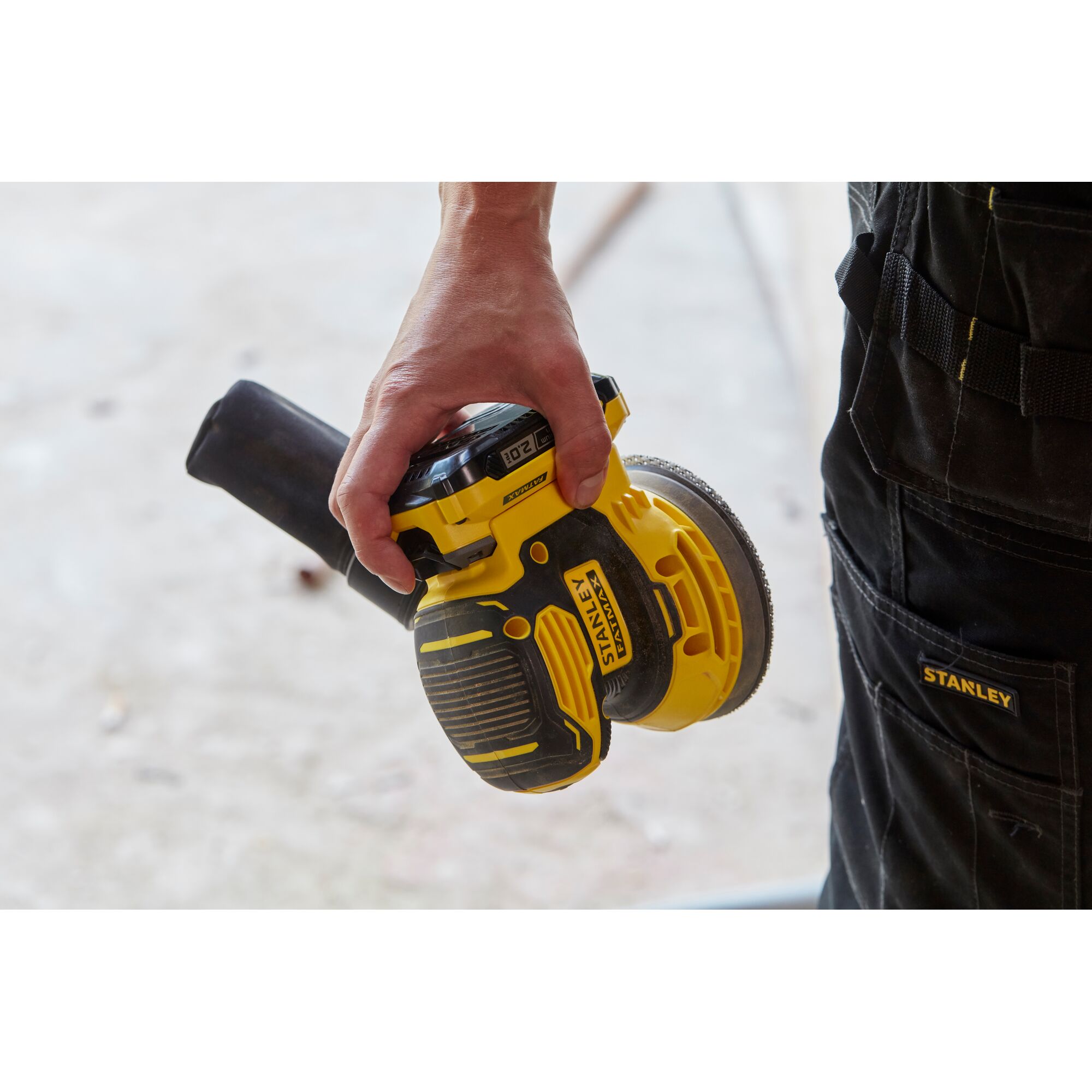 Photo of a STANLEY SCS220B cordless random orbit sander held in one hand, with clear STANLEY branding on the tool.