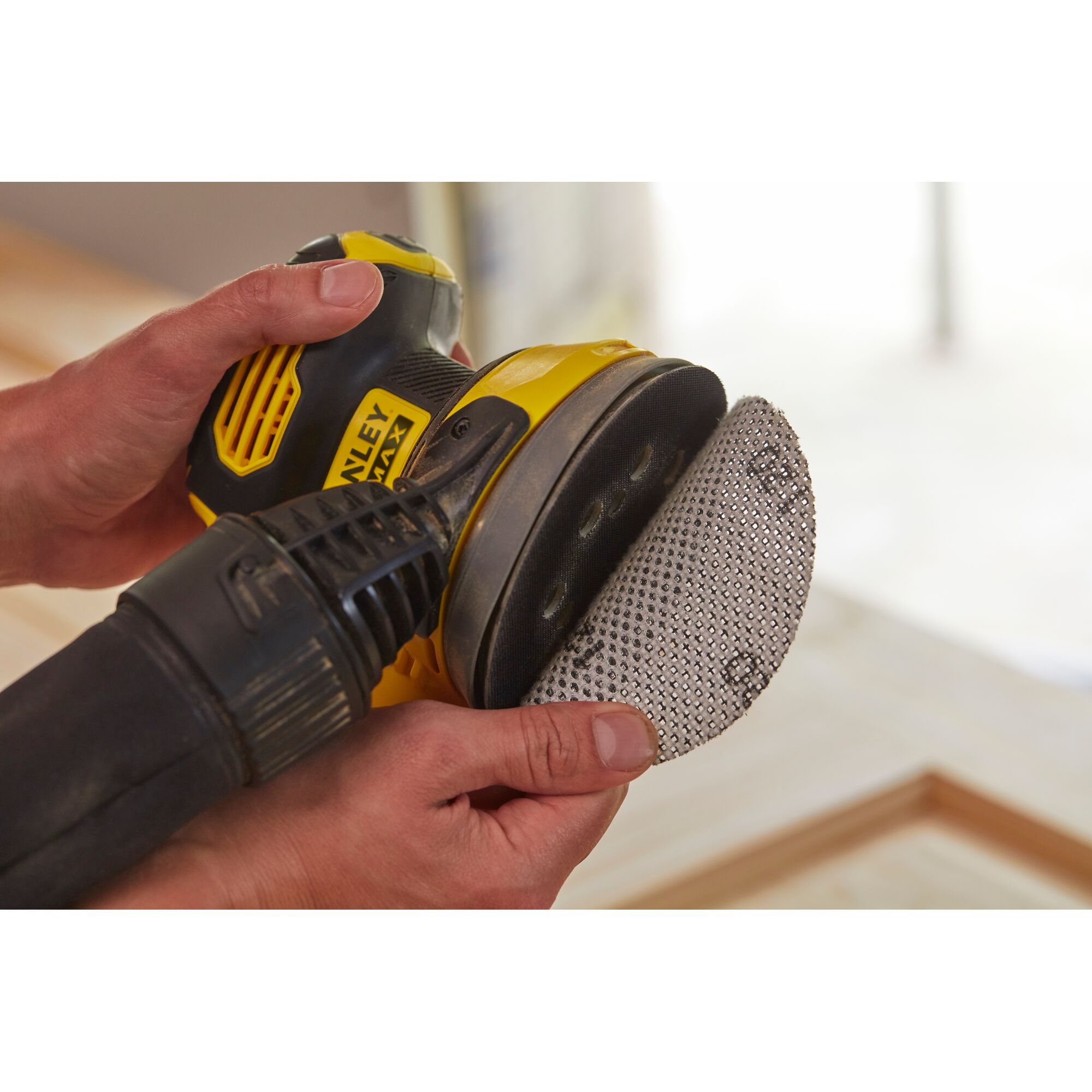 STANLEY SCS220B sander held by hands, close-up on sanding pad being attached.