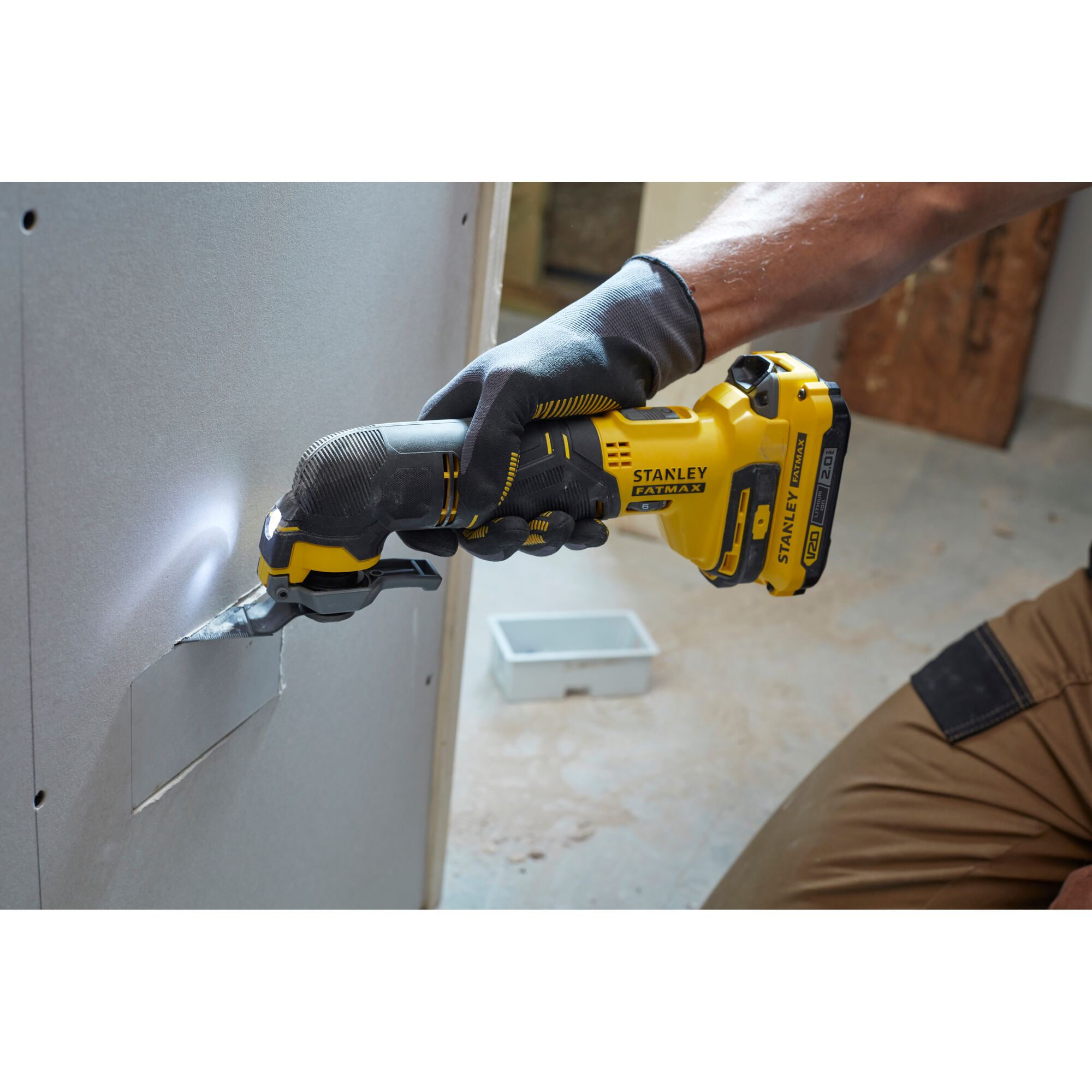 Stanley SCT500D2K oscillating tool cutting drywall, yellow and black, used by worker with gloves.
