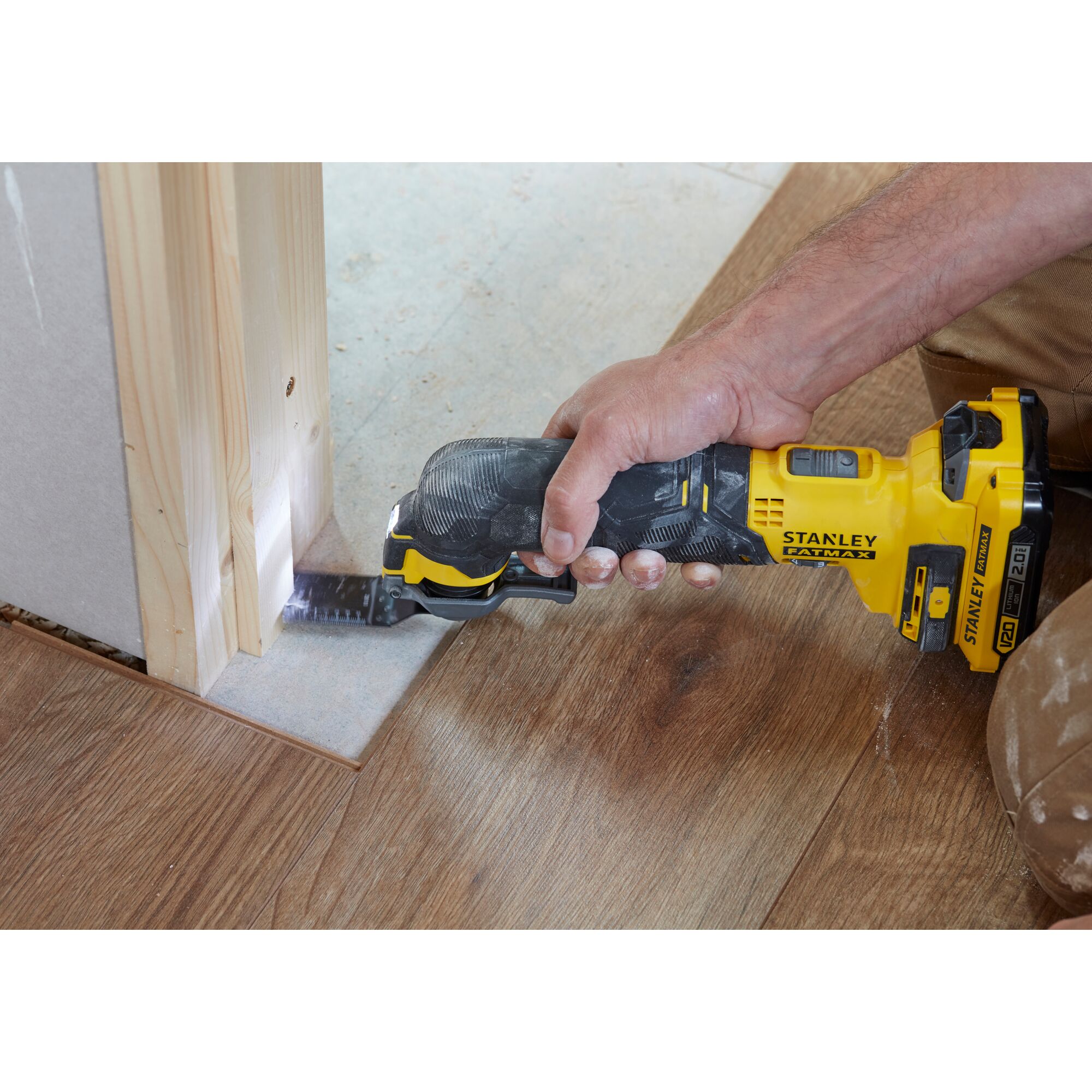 Stanley SCT500D2K oscillating tool cutting wood flooring near door frame, close-up action photo.