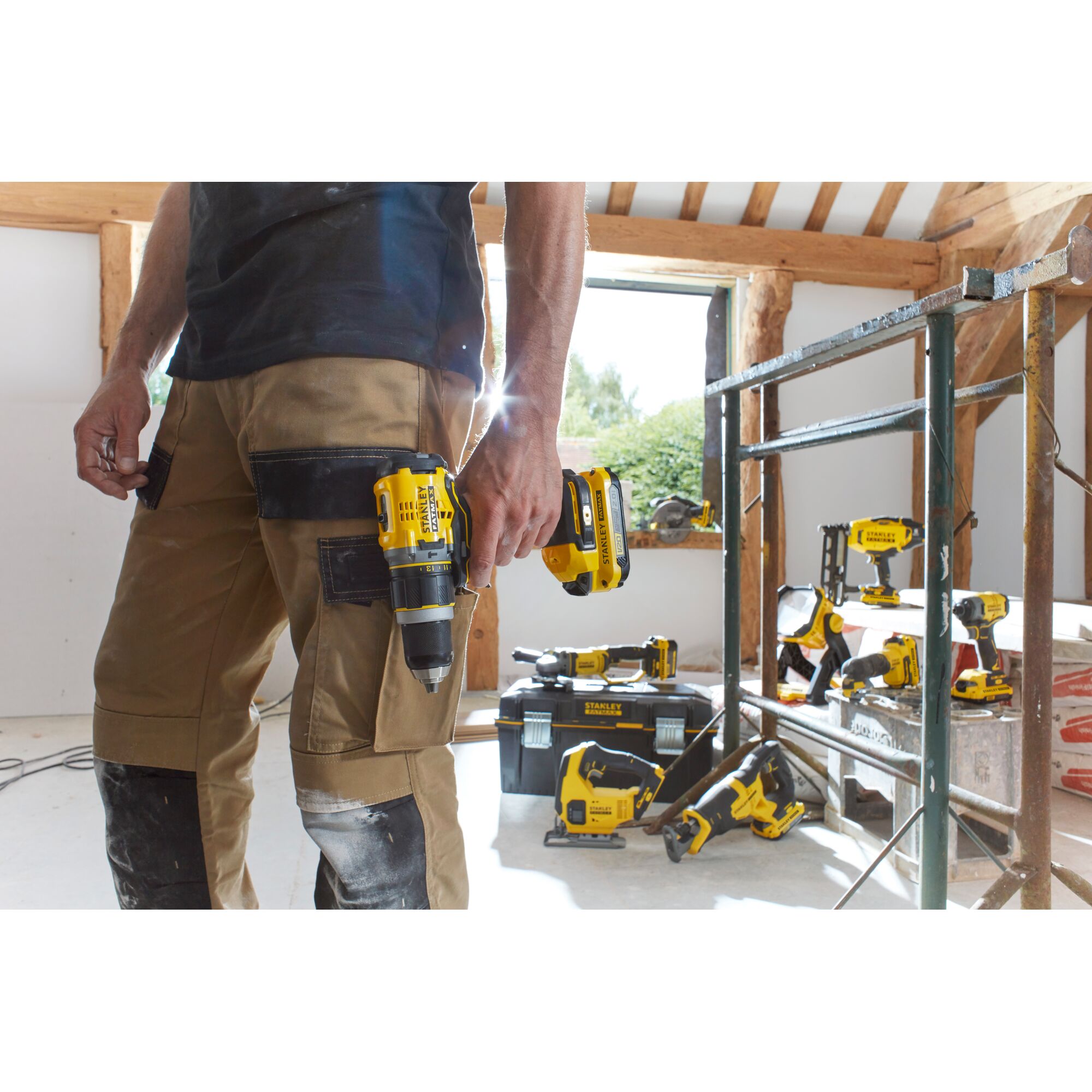STANLEY SCT500D2K cordless drill held by worker in workshop, with other STANLEY power tools and toolbox in background.