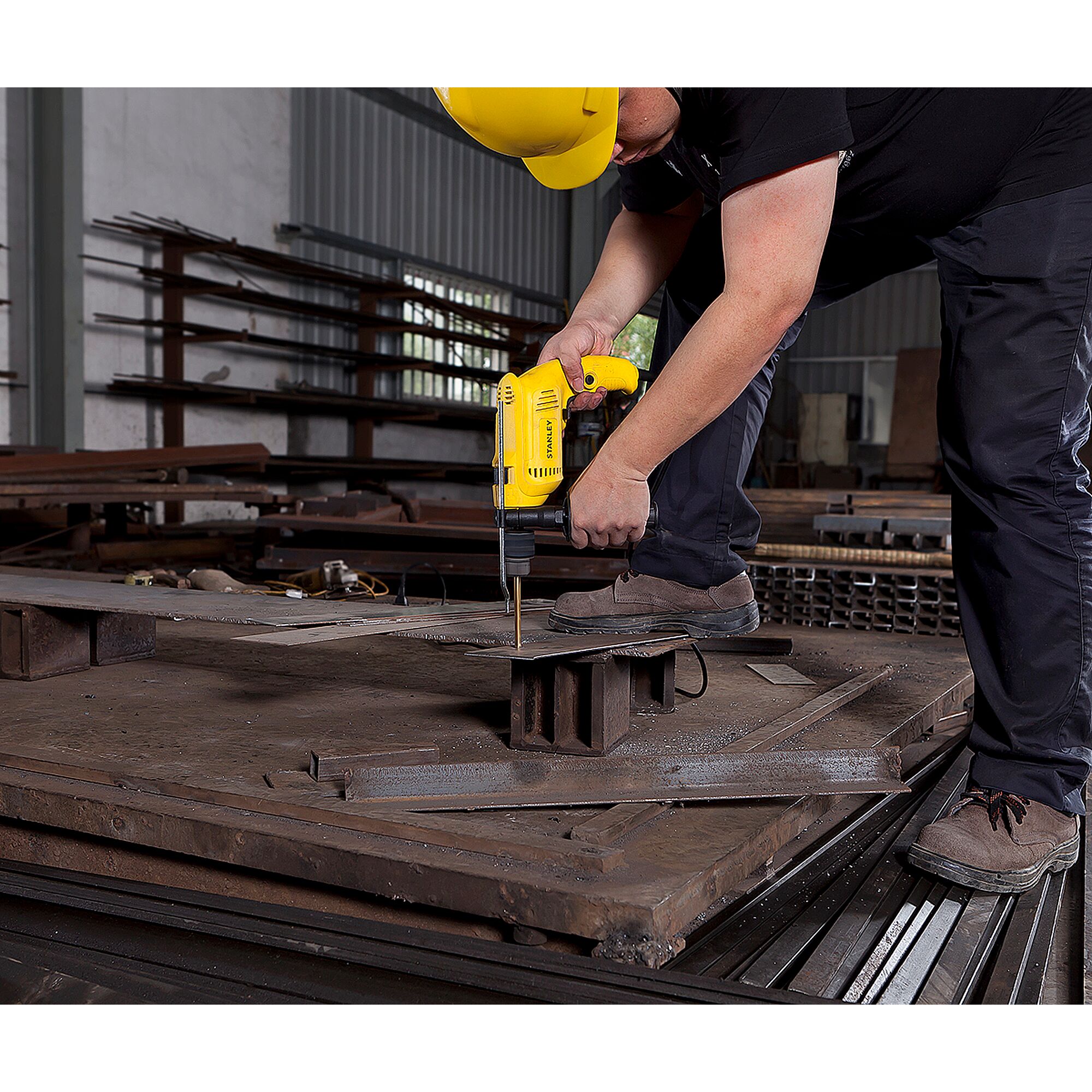 STANLEY SDH600 yellow drill being used to drill metal sheet in industrial workshop, side angle.