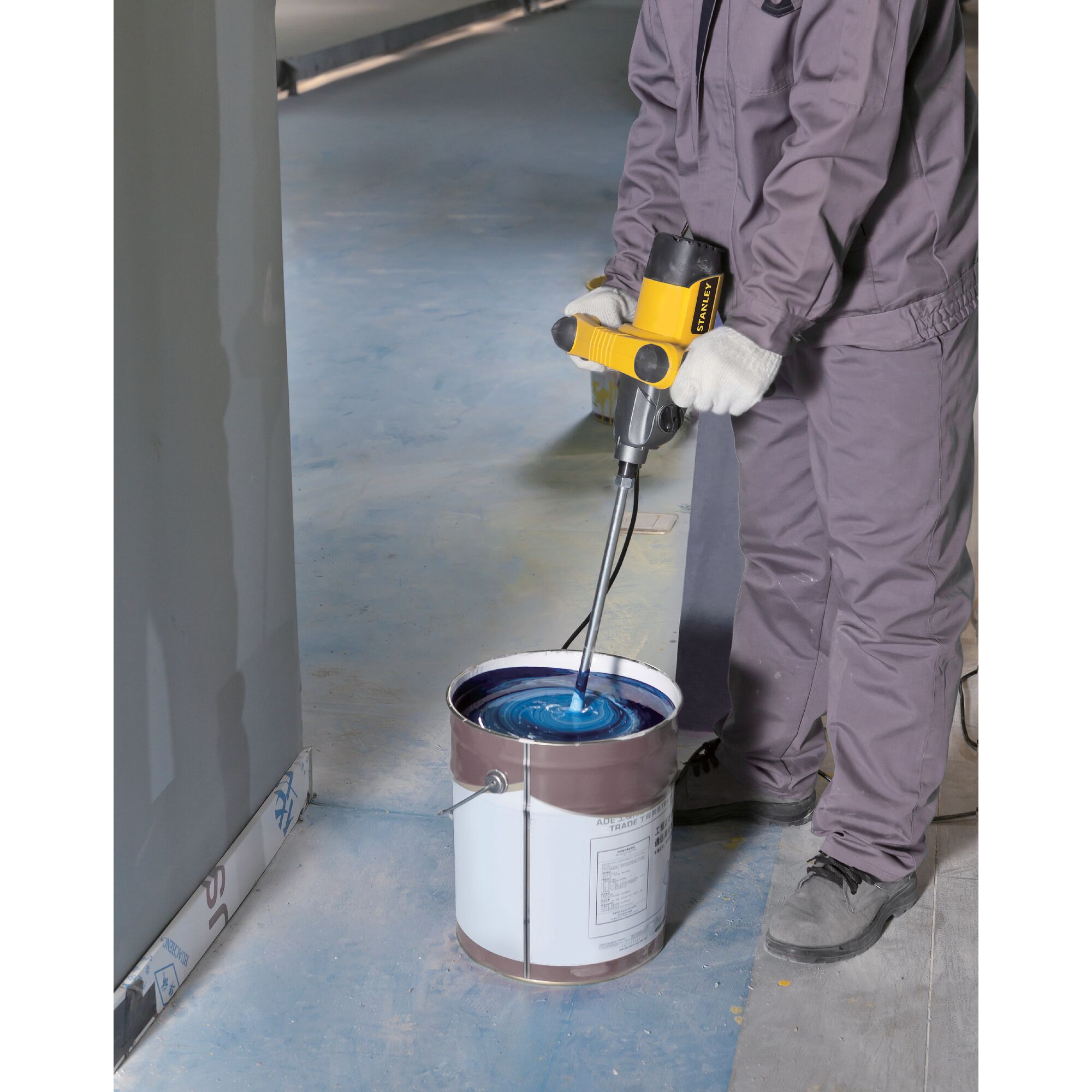 STANLEY SDR1400-KR electric mixer in use, mixing blue paint in a large bucket on a construction site floor.