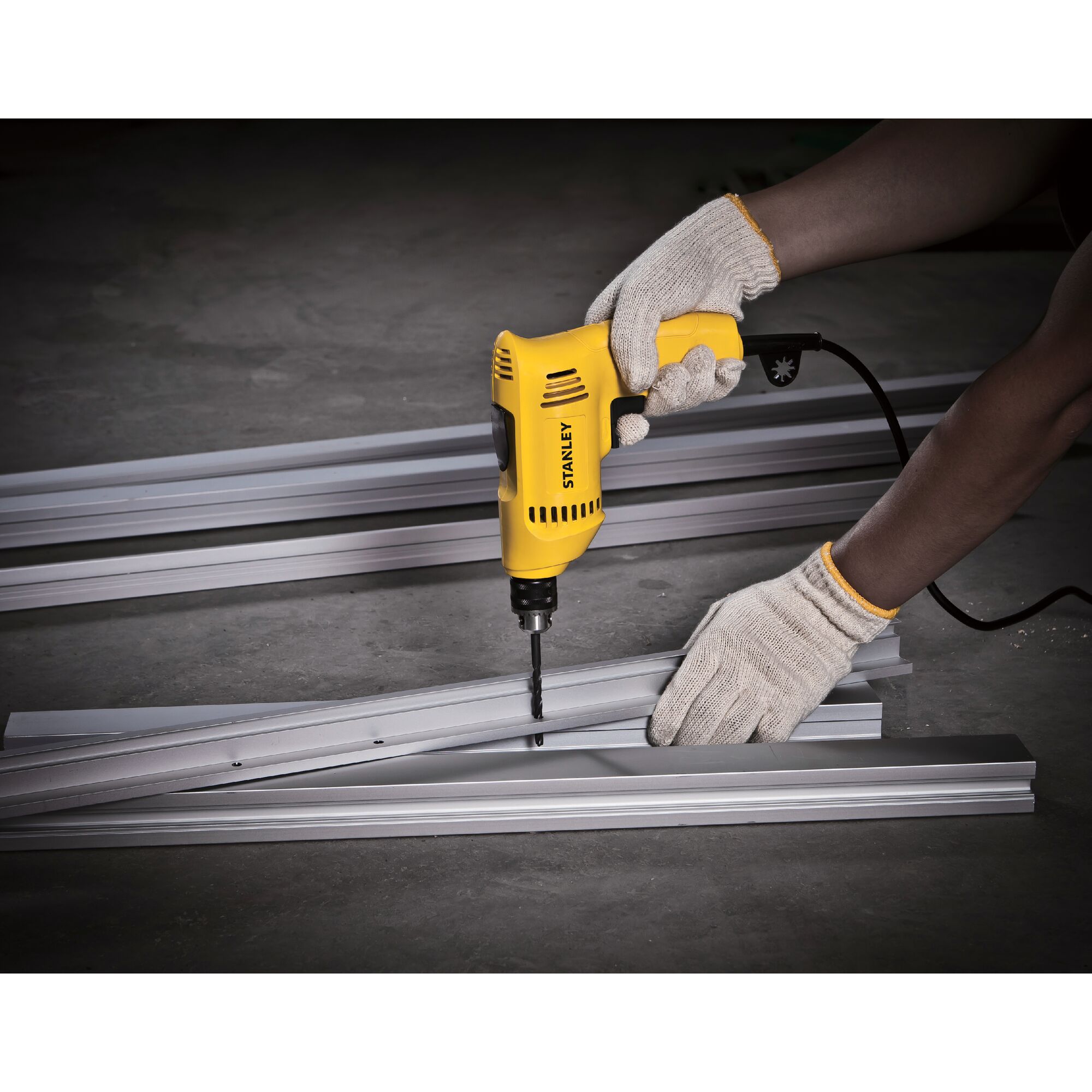 Photo of STANLEY SDR3006 electric drill in use on metal beams, worker hands with gloves, side angle.