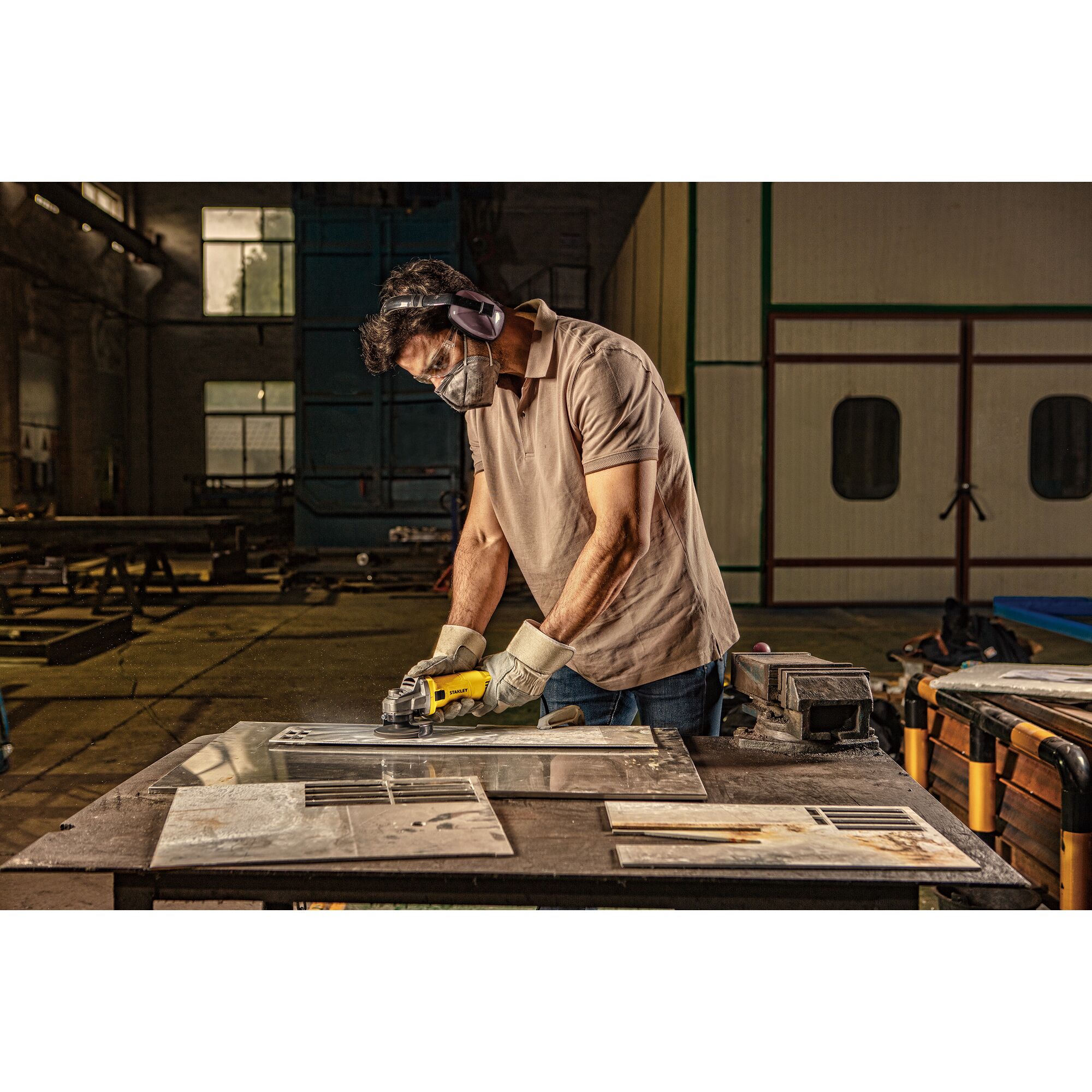 Stanley SG6100 worker using grinder on metal in workshop, side angle, safety gear worn.