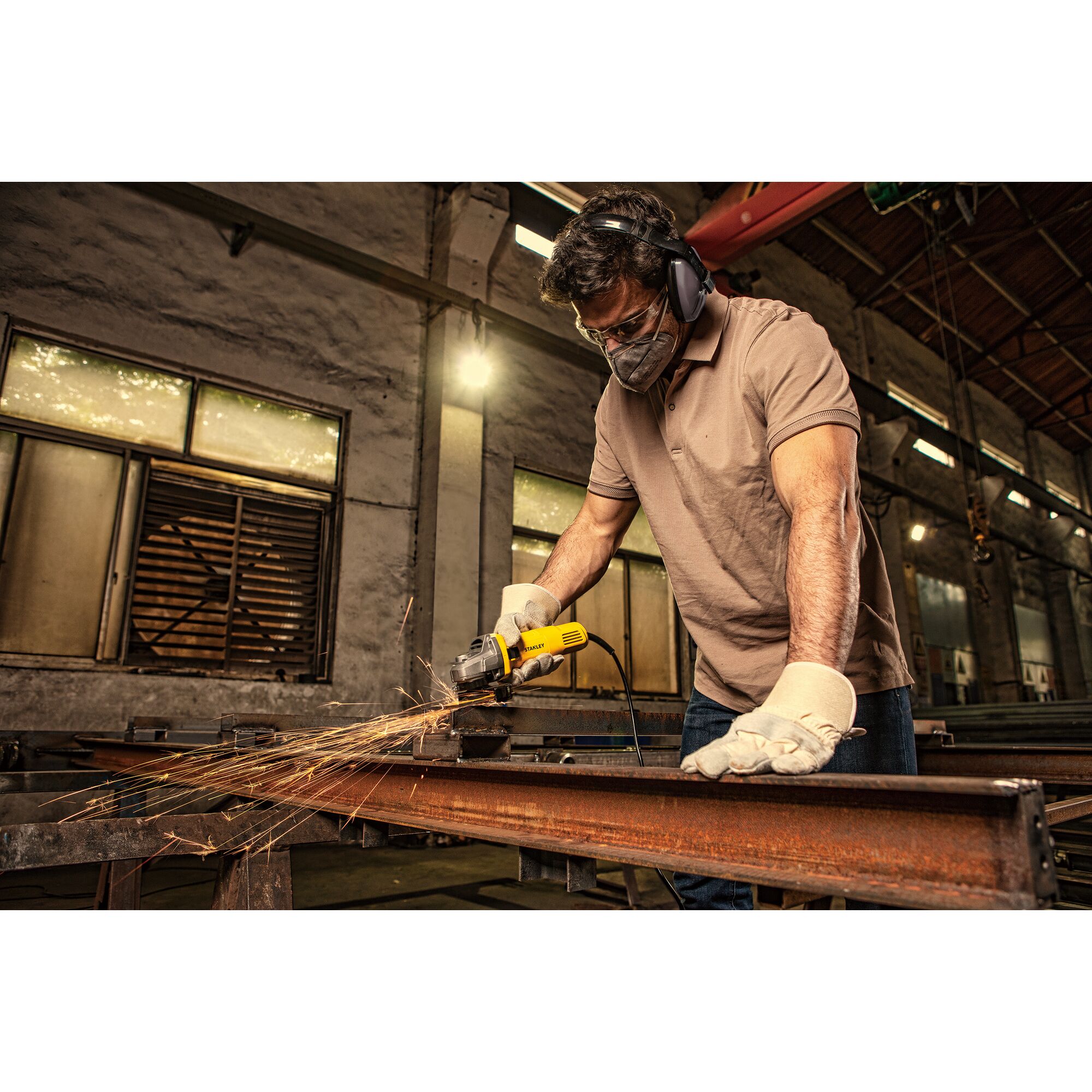 STANLEY SG6100 angle grinder in use on metal beam, sparks flying, indoor workshop setting.