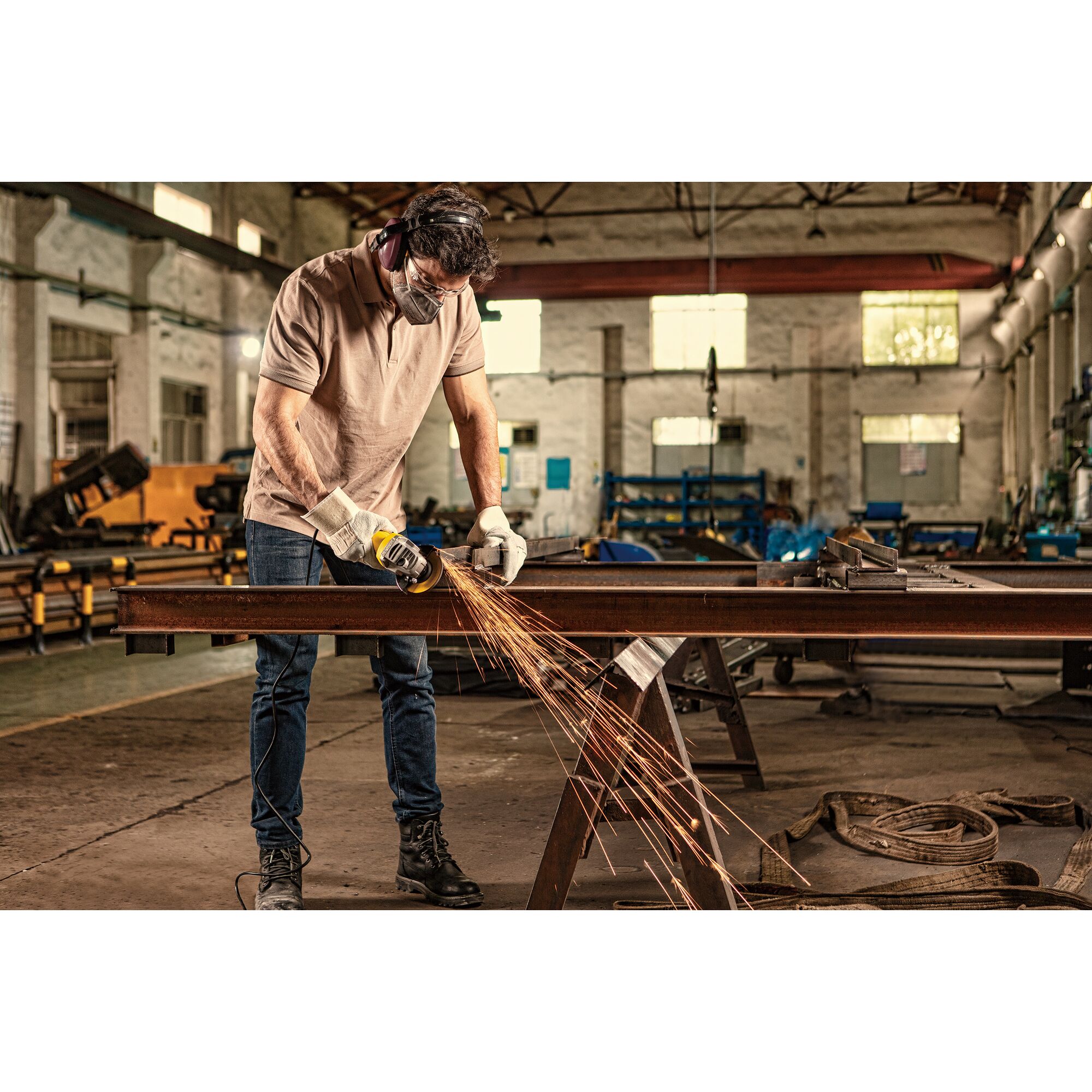 STANLEY SG7100 angle grinder used on metal beam in workshop, sparks flying, worker wearing safety gear.