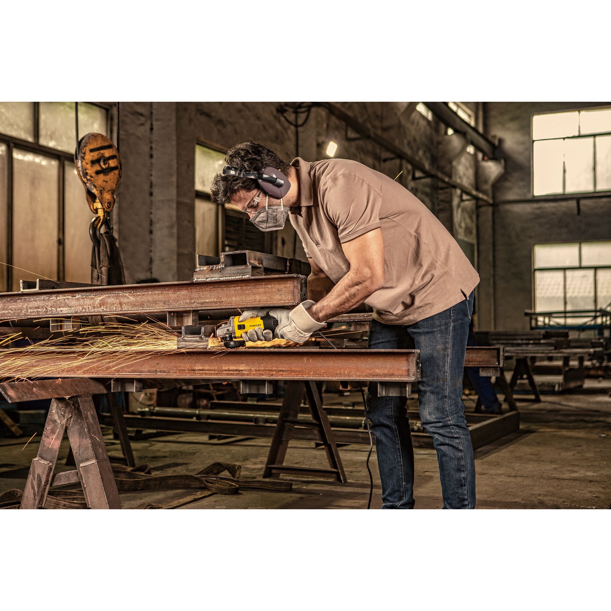 Stanley SG7100 angle grinder in use on steel beams in industrial workshop, side view.