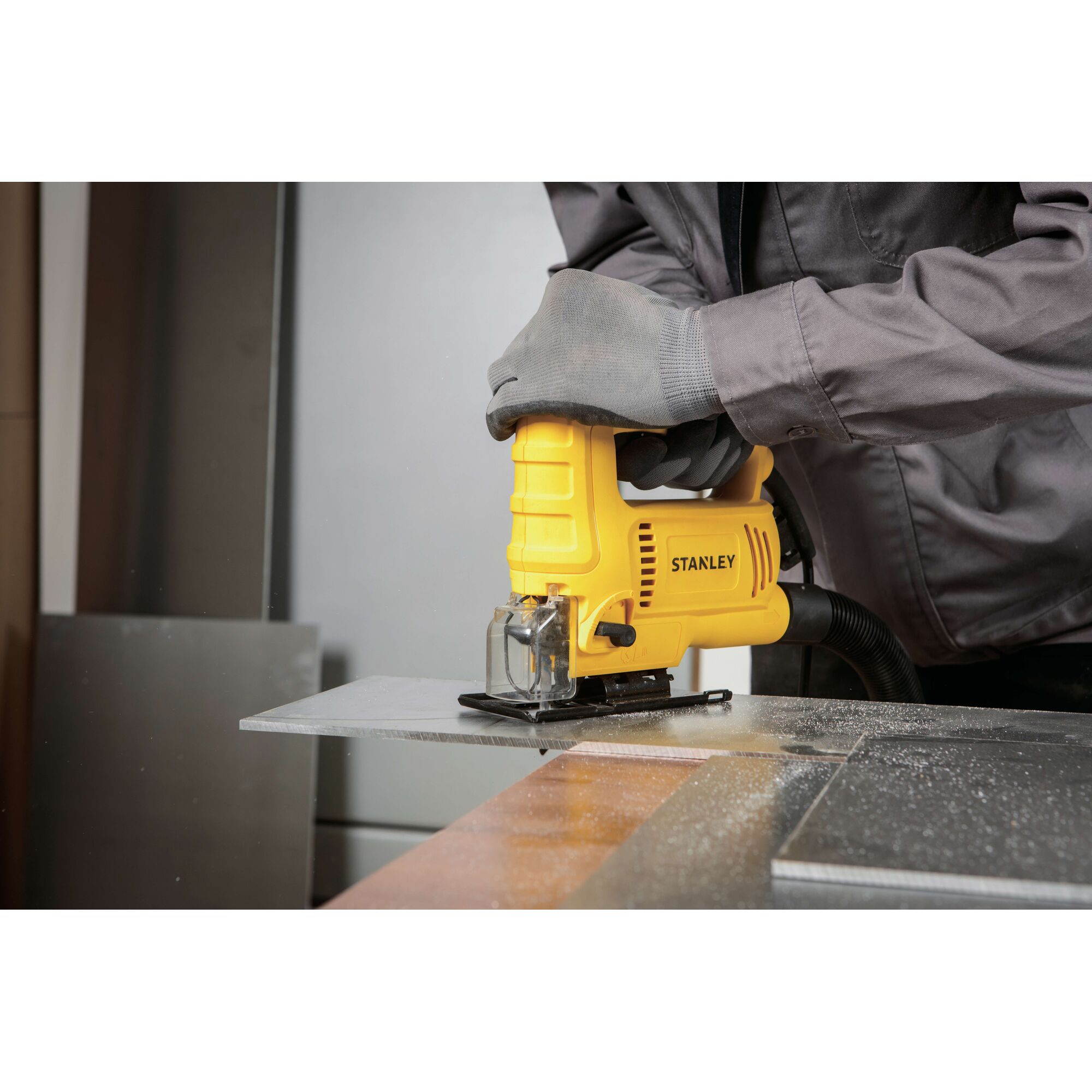 Stanley SJ60 jigsaw cutting metal sheet, yellow tool held with gloves, photo in workshop.