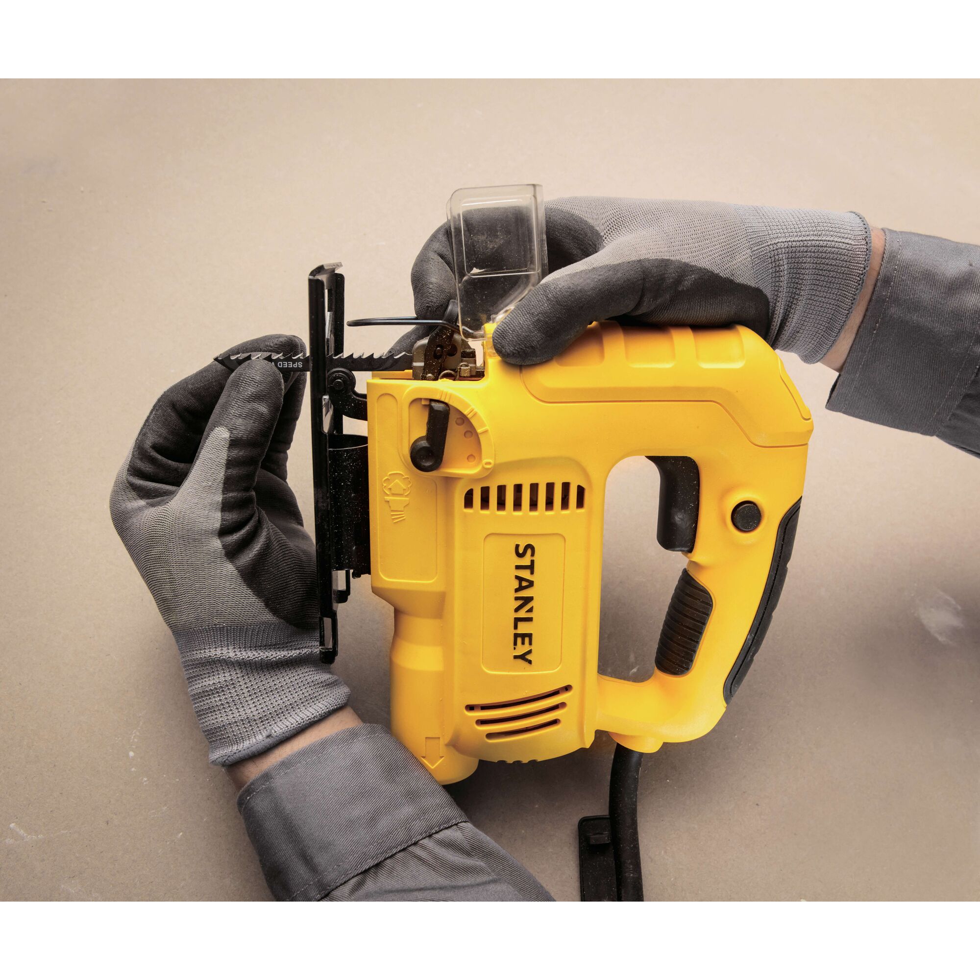 Photo of STANLEY SJ60 jigsaw, yellow body, being loaded with a blade by gloved hands, close-up view.