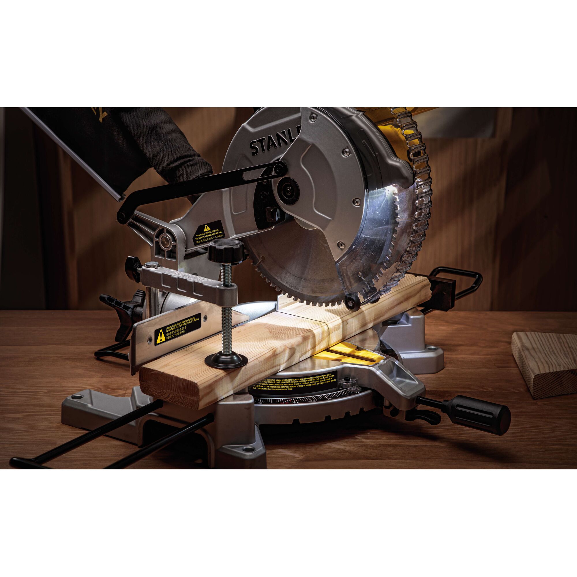 STANLEY SM16-B3 miter saw cutting wood, side angle, silver blade, mounted on wooden workbench.