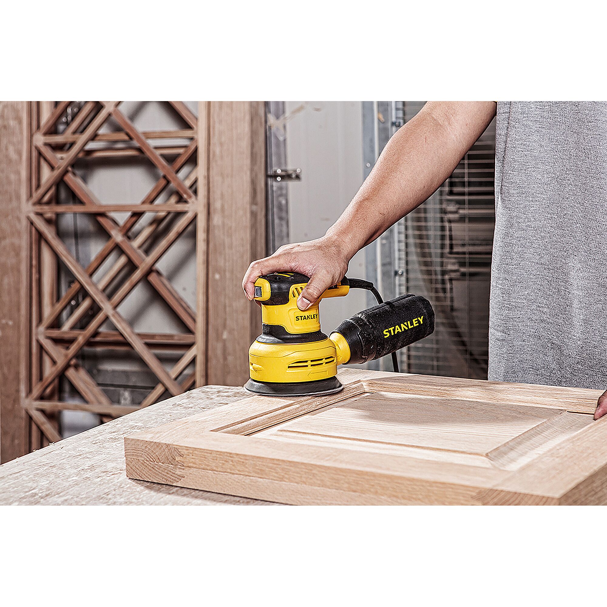 STANLEY SS30-B2C random orbital sander shown sanding a wooden cabinet door in a workshop.