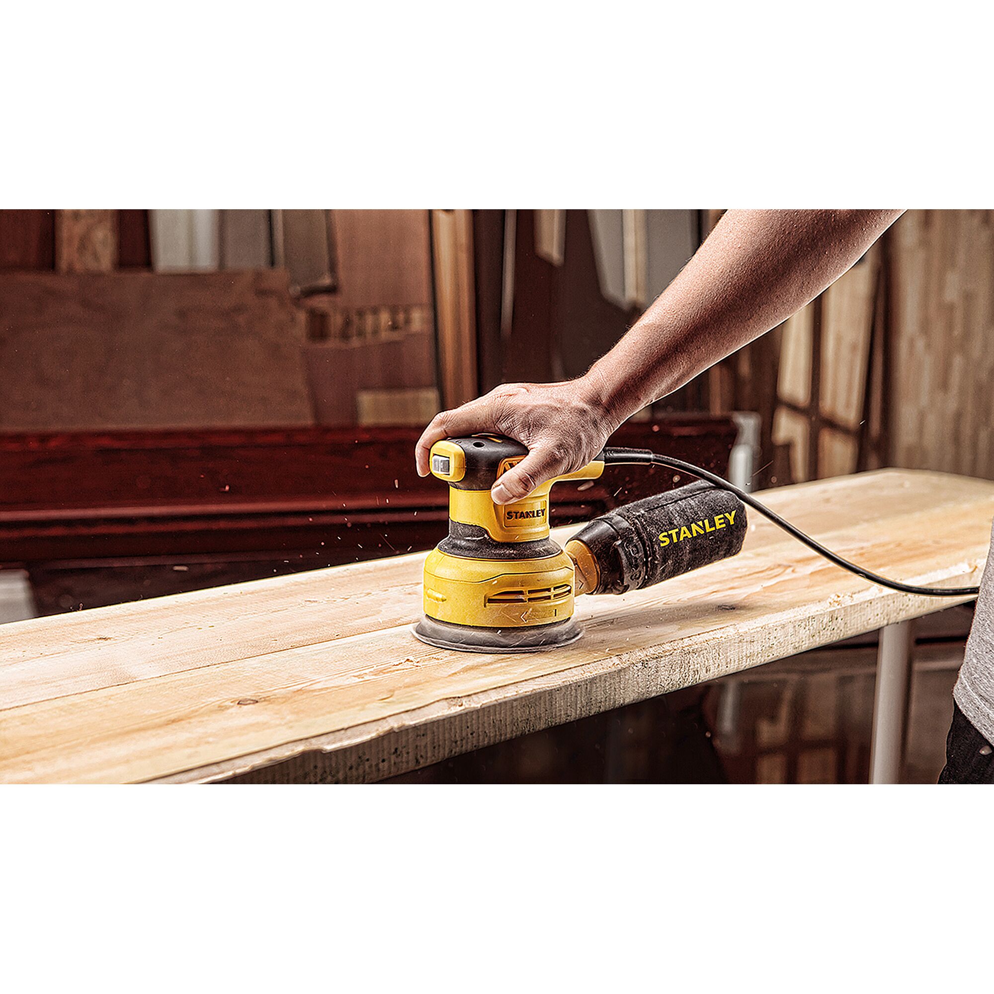 Photo of STANLEY SS30-B2C random orbital sander in use on wooden plank, handheld, dust bag attached.