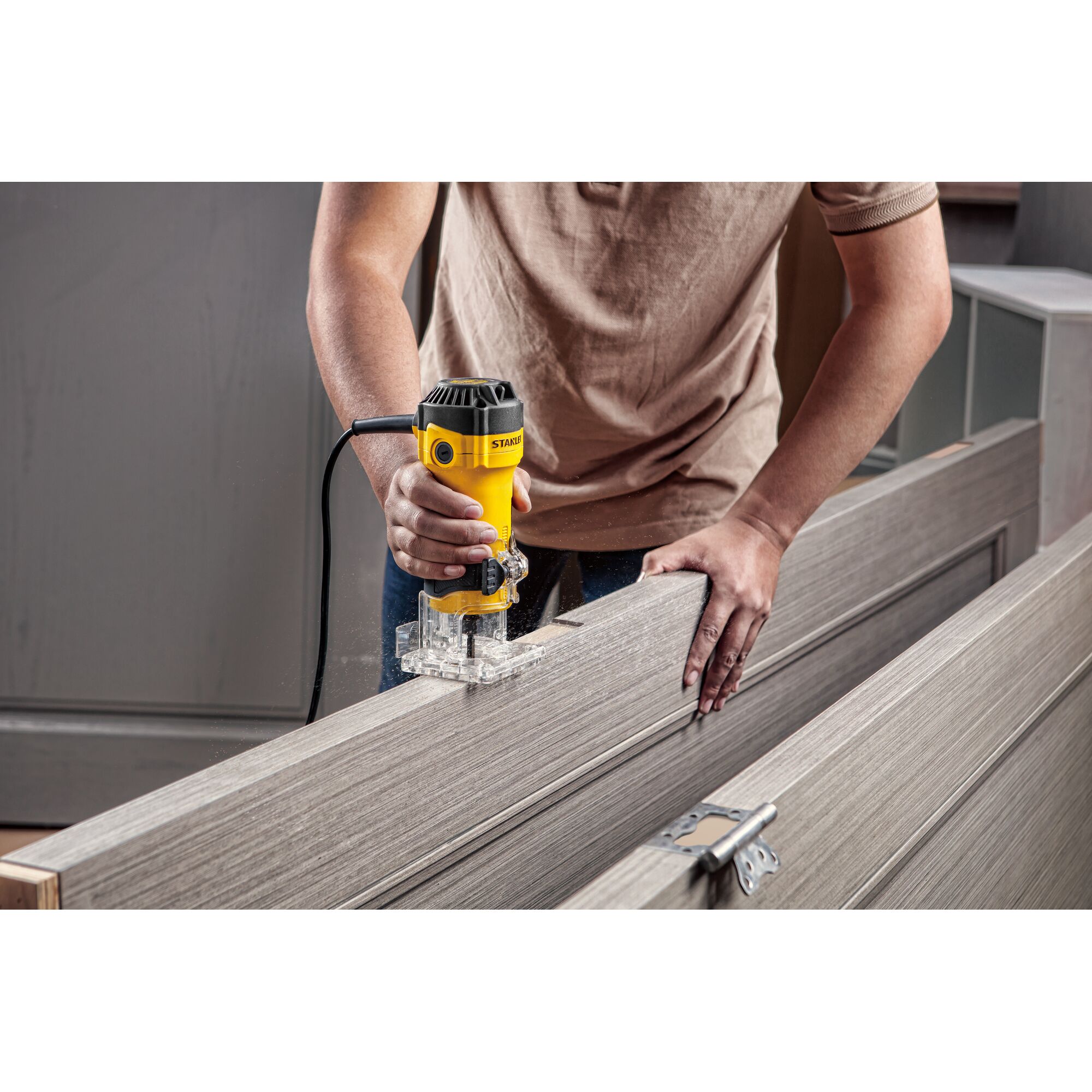 Photo of STANLEY ST55-B2 compact router being used on a wooden door, clear base, user holding tool with one hand.