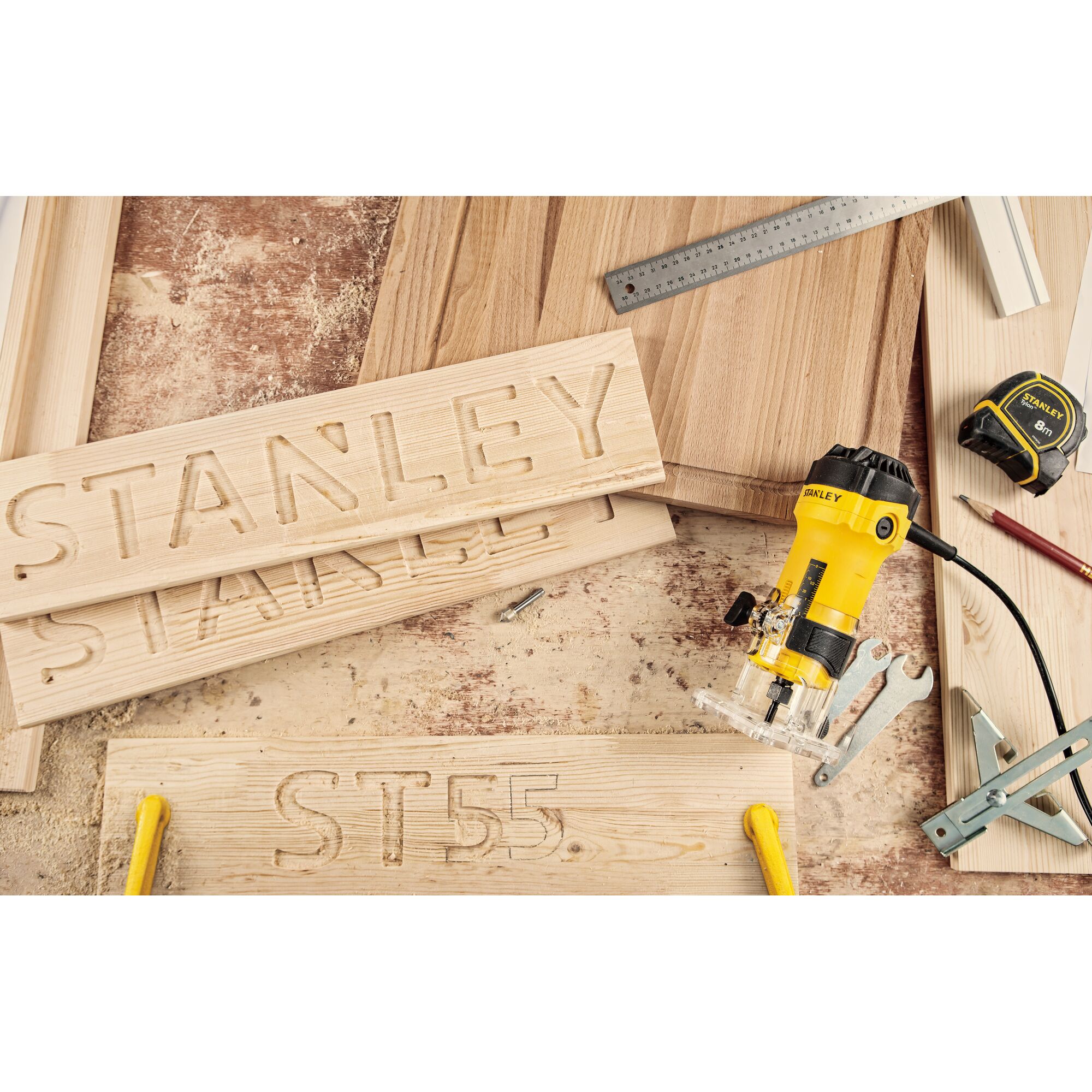 STANLEY ST55-KR woodworking router with engraved wood boards, tape measure and tools, top angle photo.