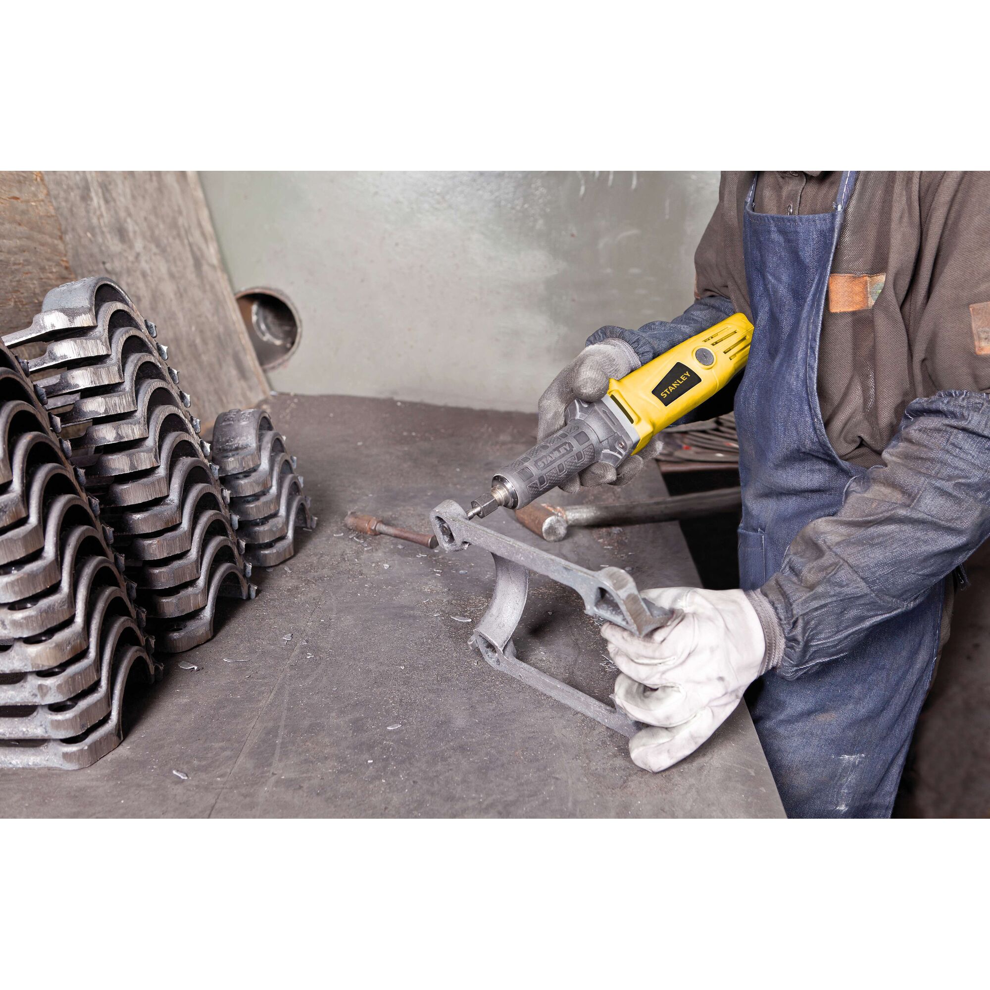 STANLEY STEL861 rotary tool used on metal part in workshop, person wearing gloves and apron.