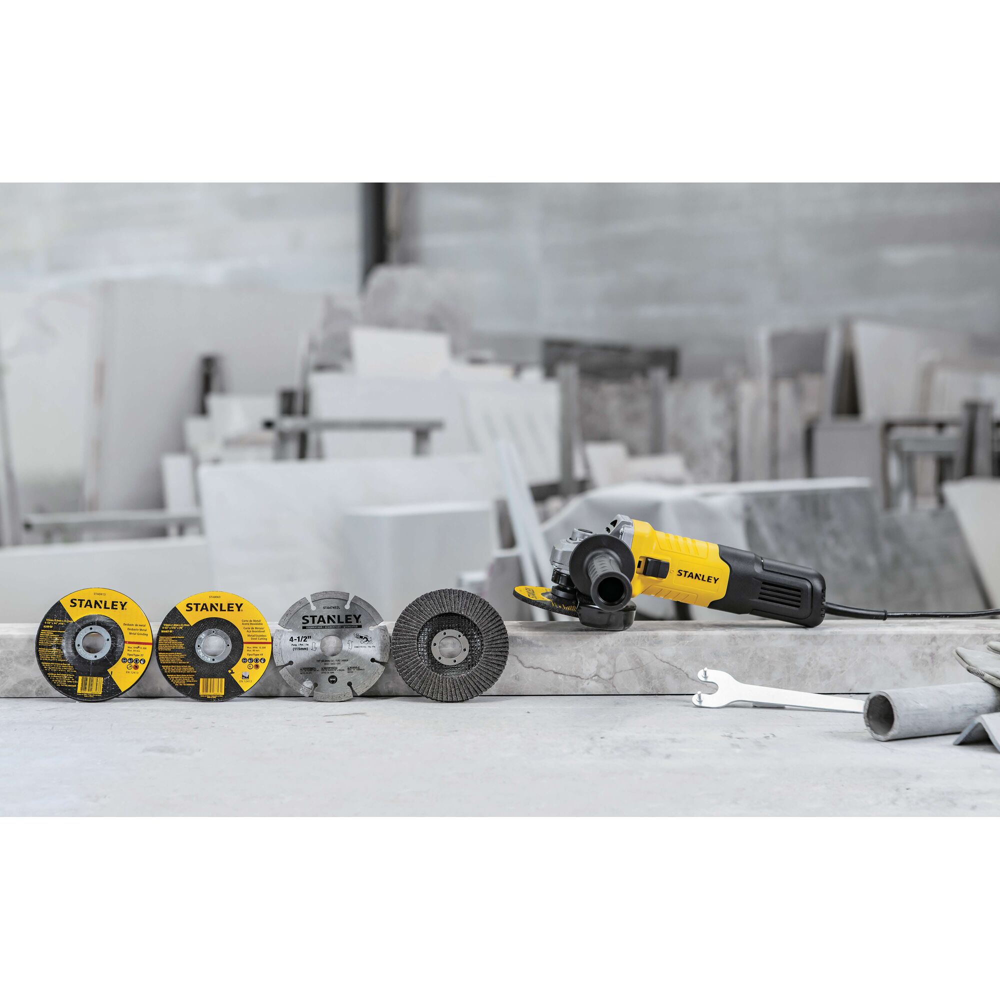 STANLEY STGS9100 angle grinder with four grinding discs and wrench on a stone surface, side view.
