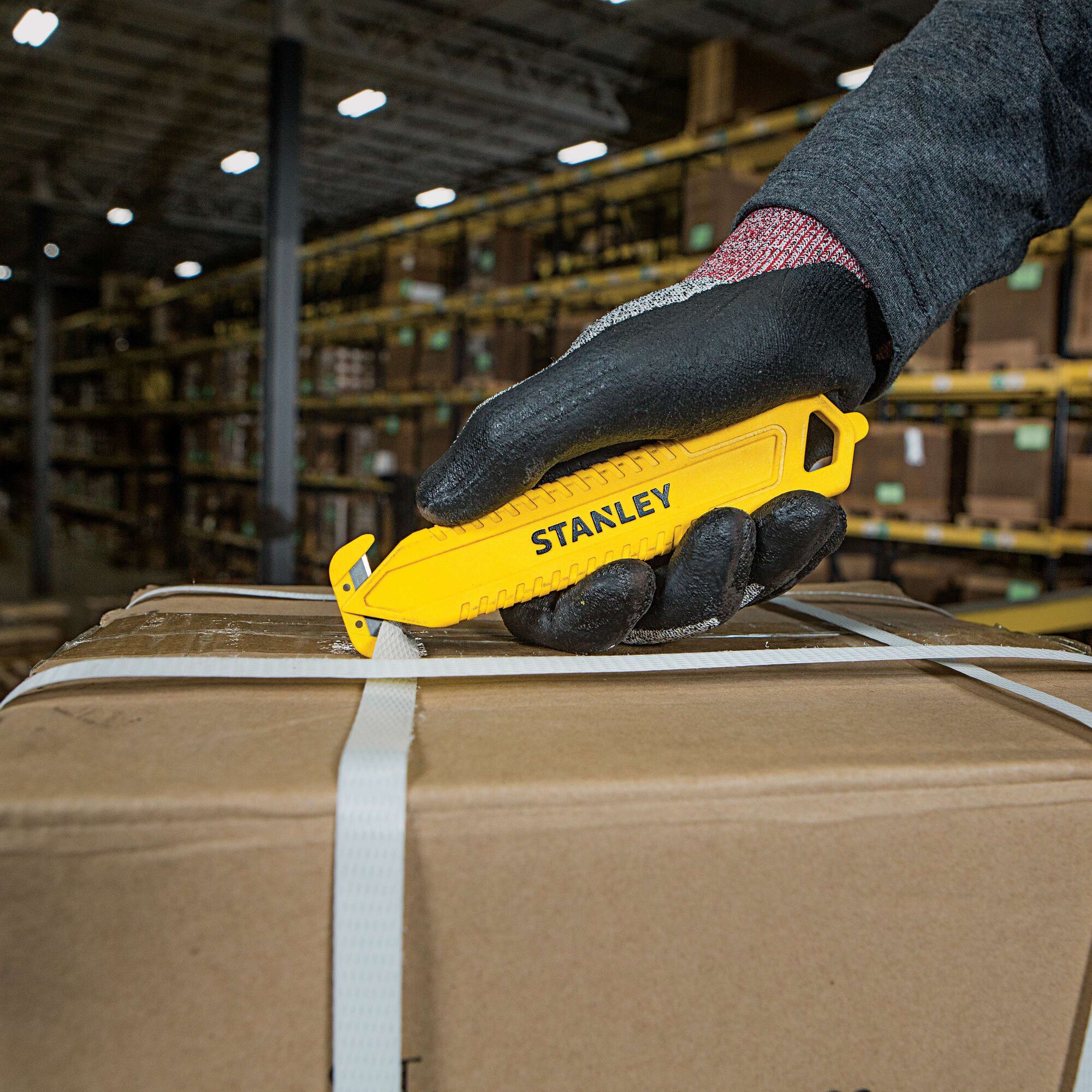 Stanley STHT10359 yellow safety knife cutting box strap in warehouse, close-up photography.