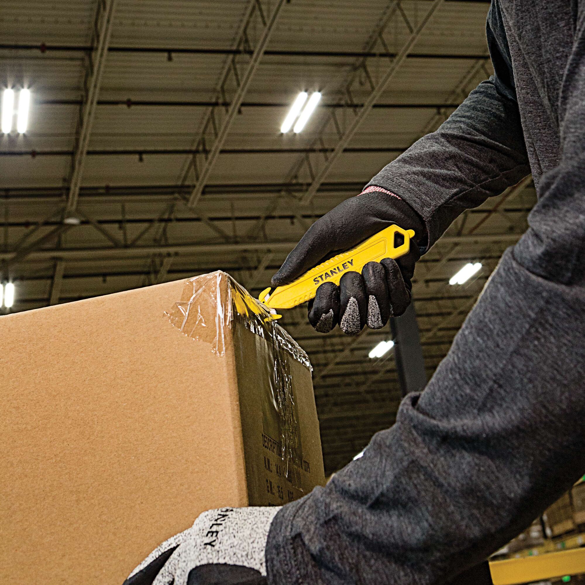 STANLEY STHT10359 utility knife cutting tape on a cardboard box, worker wearing black gloves.