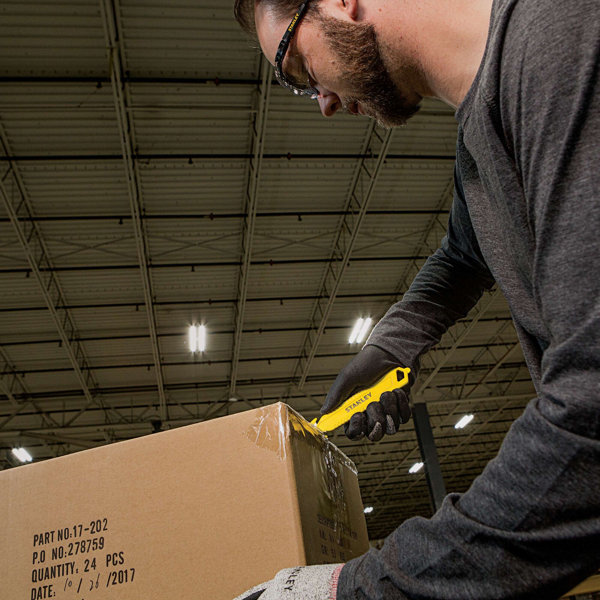 Stanley STHT10359 yellow utility knife cutting box tape in warehouse, close-up side angle.