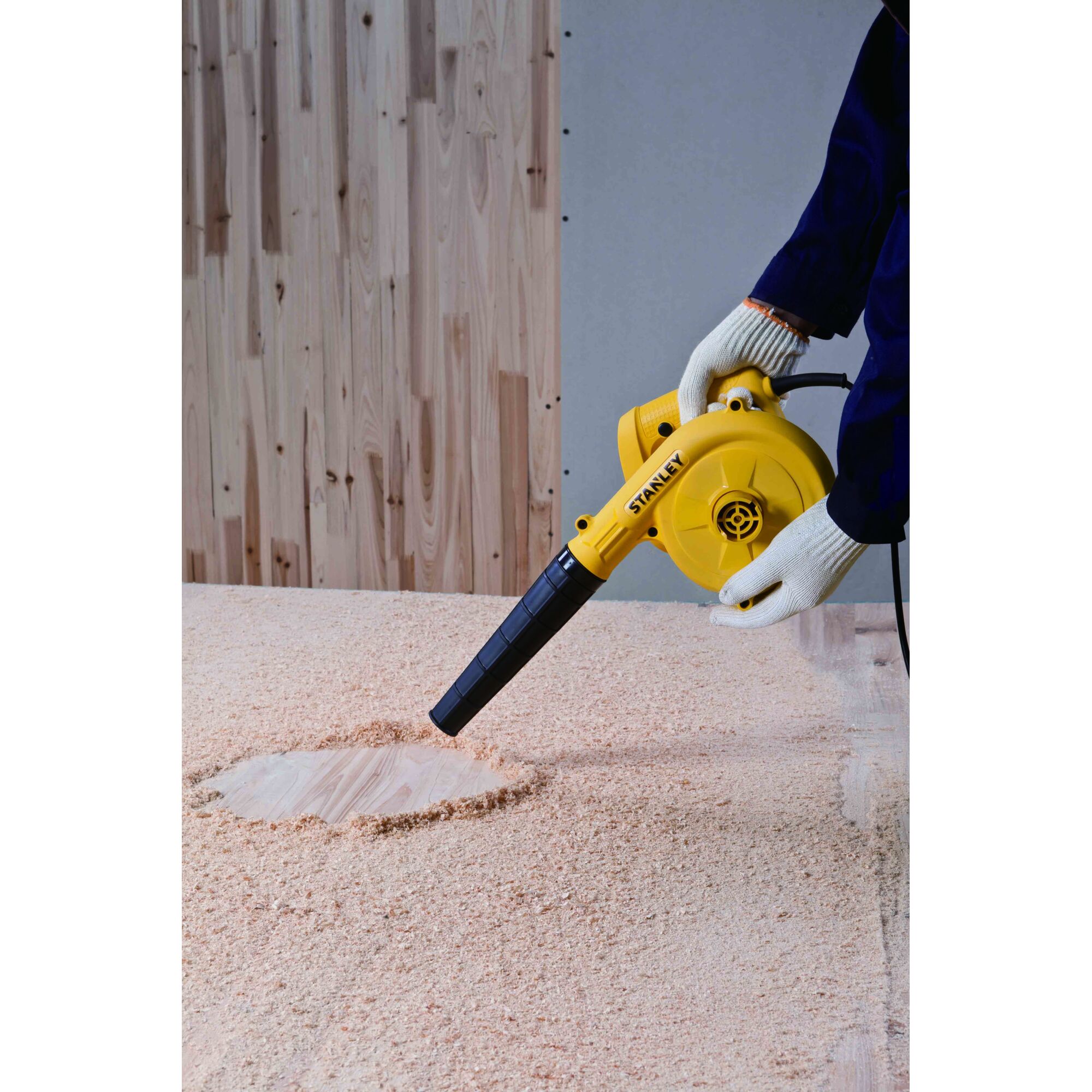 Photo of STANLEY STPT600-KR yellow electric blower being used to clear sawdust from wooden surface, front angle.